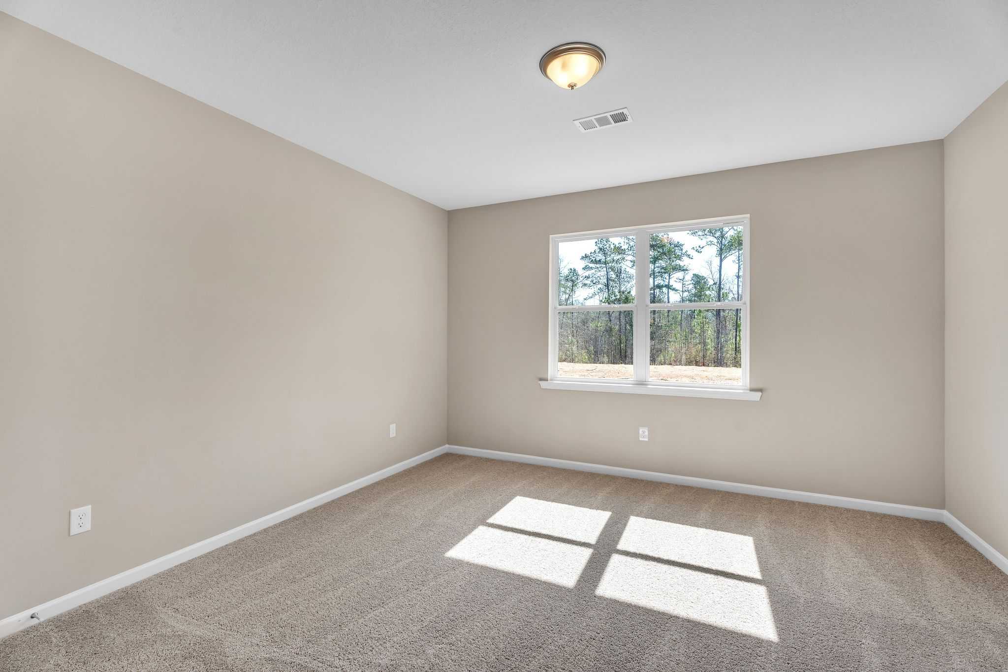 Spacious empty bedroom with beige walls, carpet flooring, and large window overlooking pine trees at Anderson Lakes in Opelika, Alabama