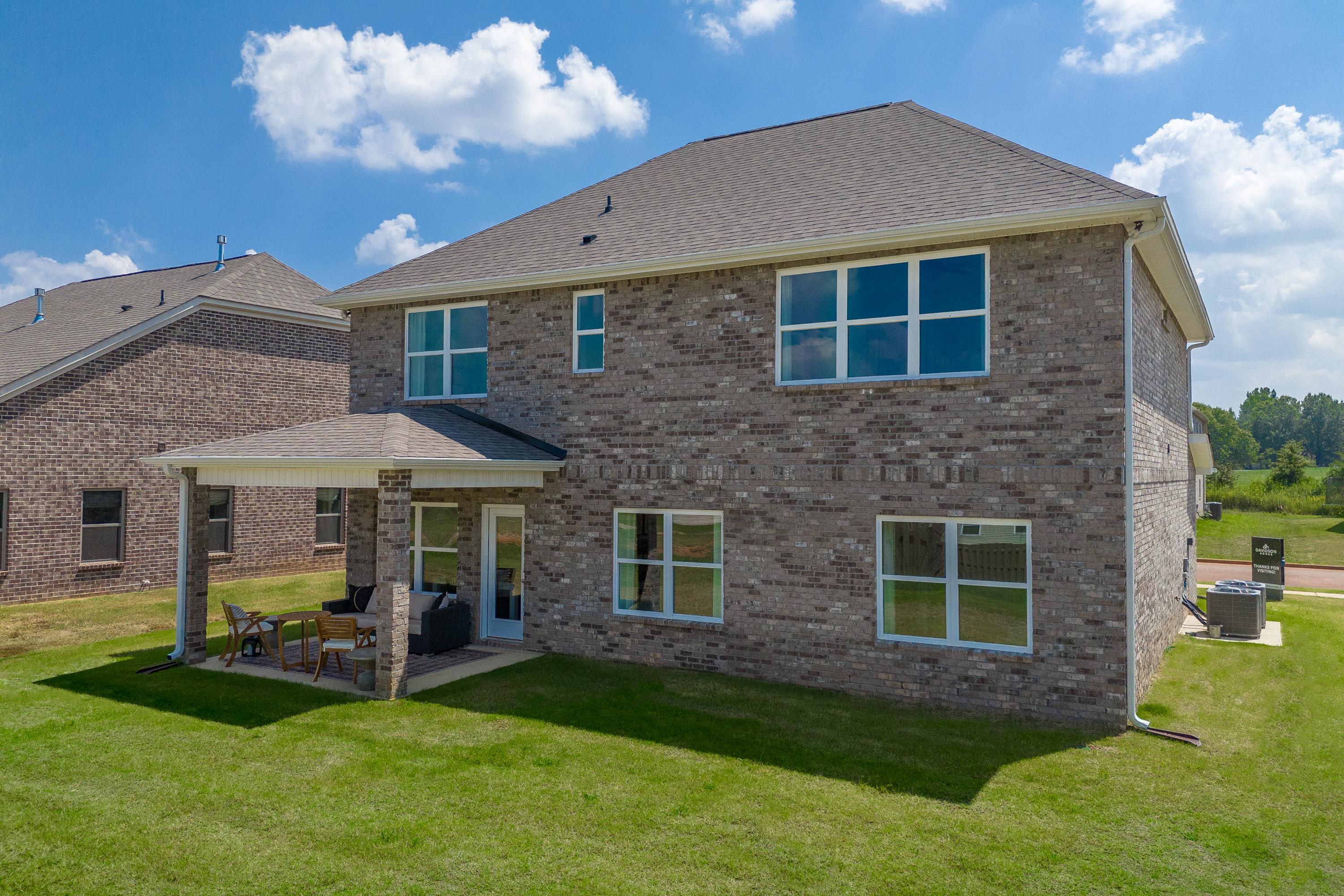 Rear elevation of The Shelby A two-story brick home with covered patio, large windows, and green lawn in Meridianville