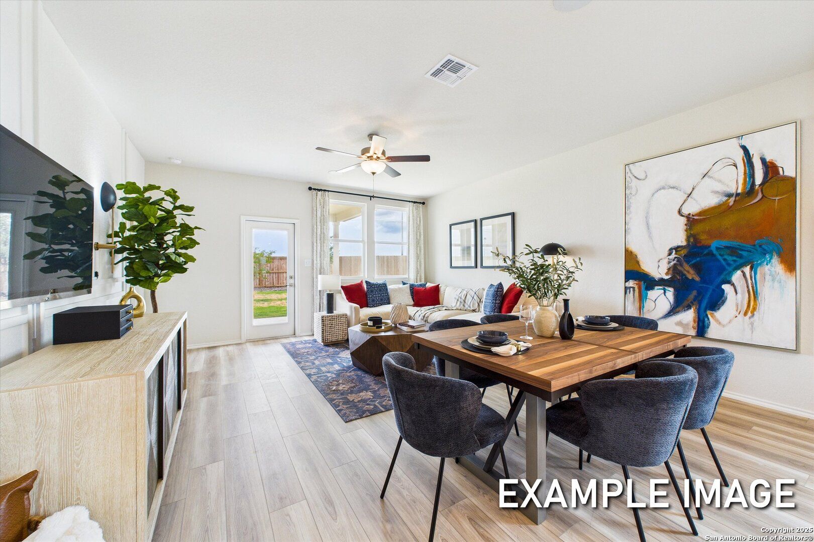 Spacious open living-dining area with modern TV console, abstract art, wooden table, and large windows in Davidson Homes The Brazos C, San Antonio