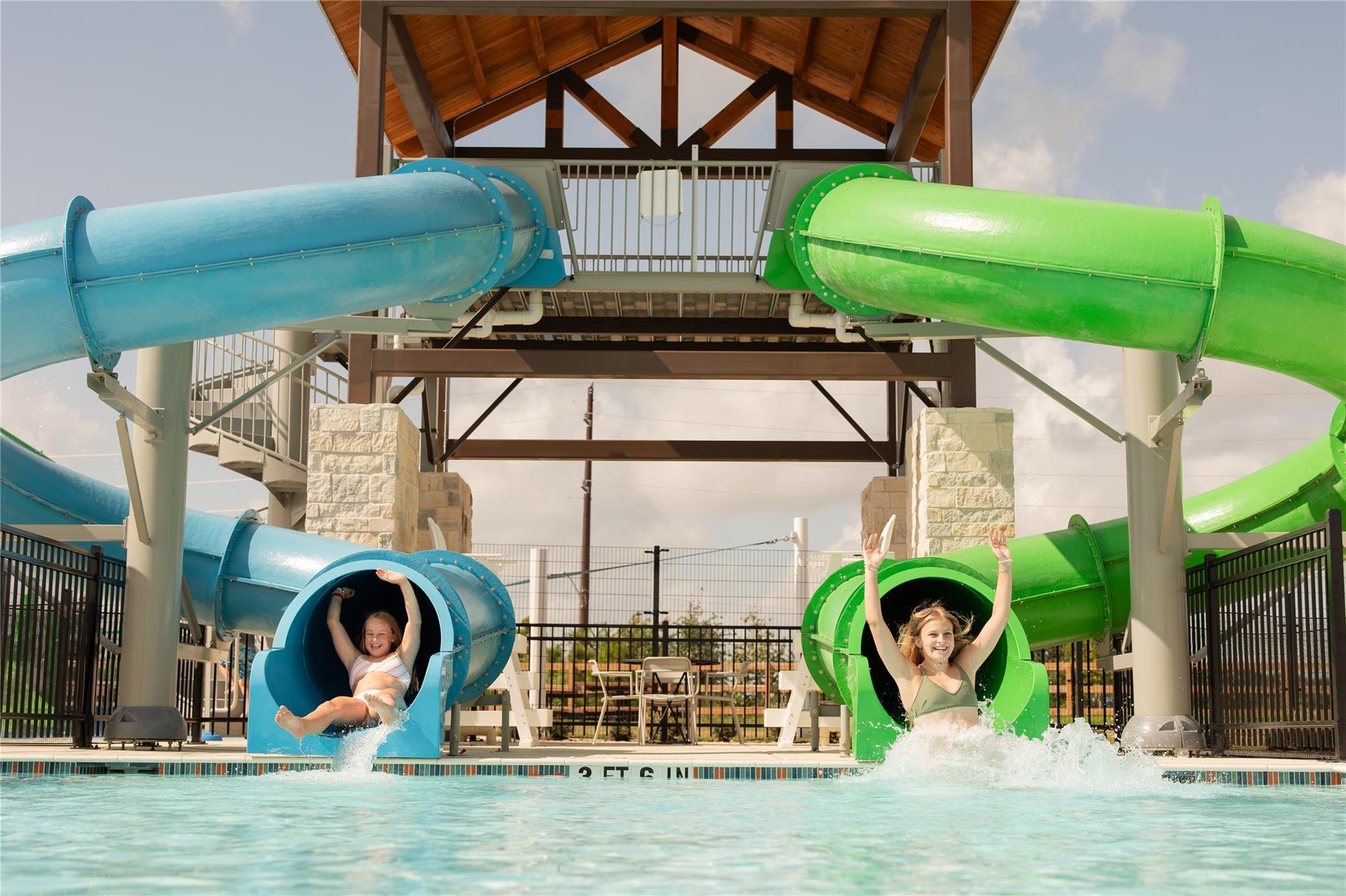 Two women sliding down blue and green waterslides into community pool at Emberly, Beasley, Texas