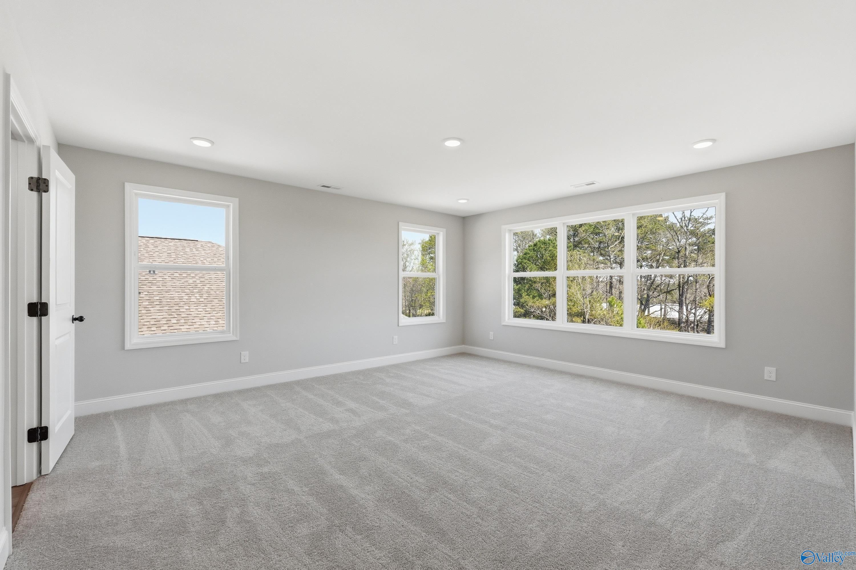 Spacious empty bedroom with large windows overlooking trees, gray carpet and neutral walls in Davidson Homes The Chelsea D, Cullman AL