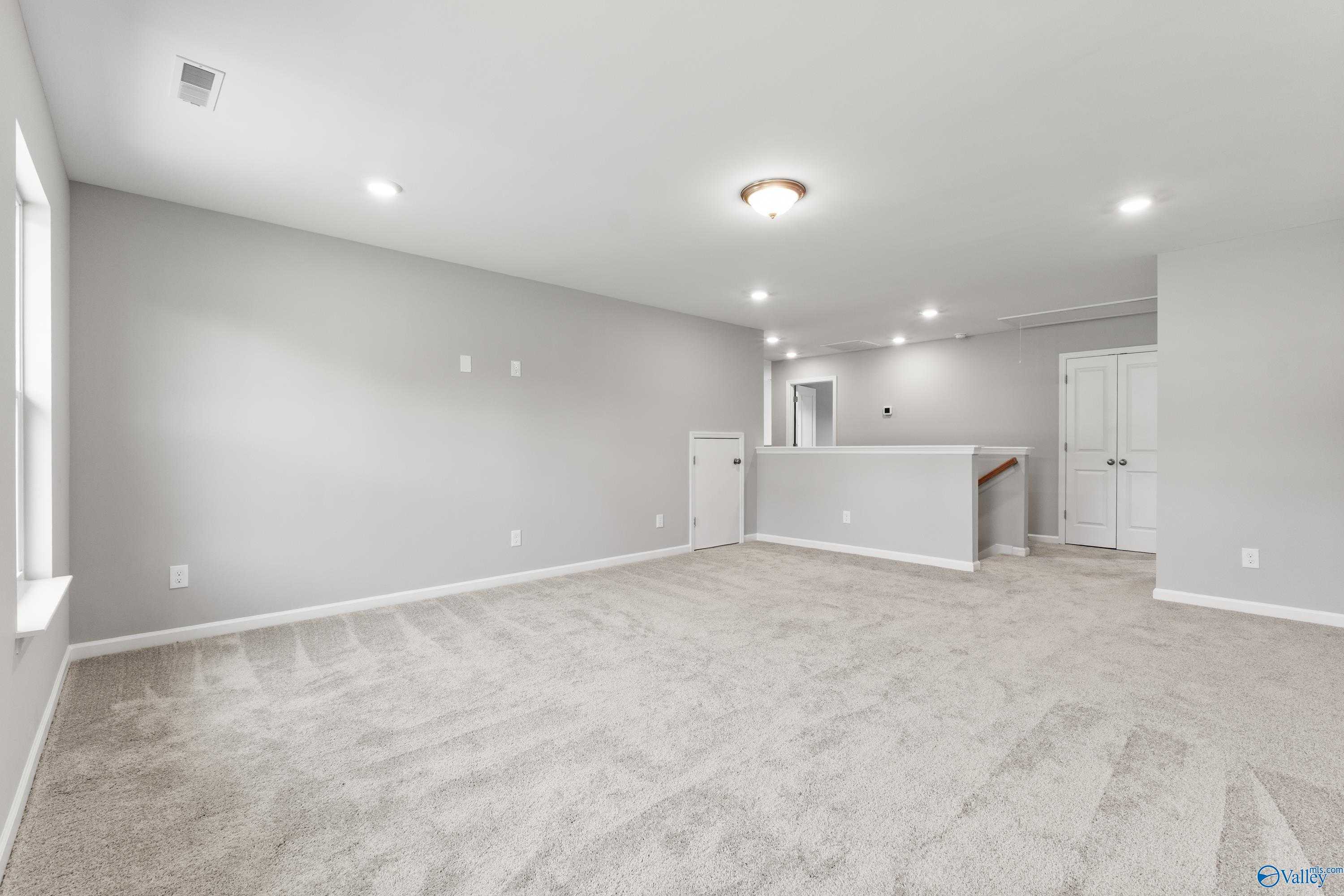 Spacious upstairs loft with gray walls, beige carpet, staircase railing, and recessed lighting in Davidson Homes The Charm, Huntsville