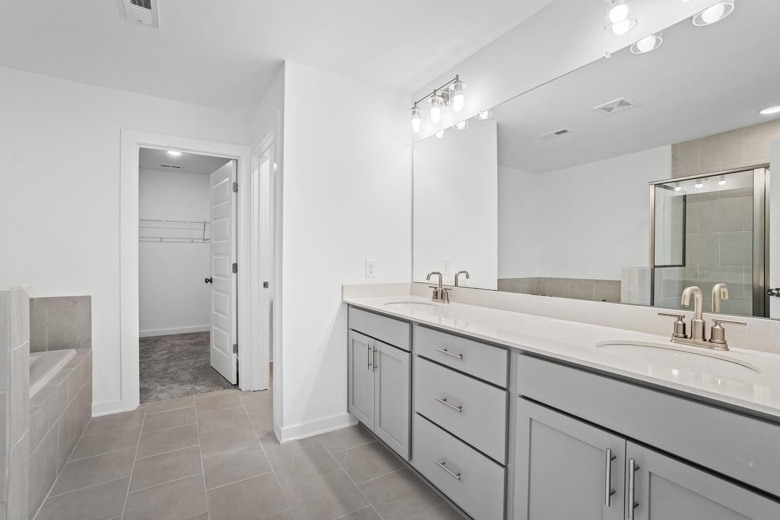 Modern primary bathroom with dual vanity, large mirror, and walk-in closet in The Logan B floor plan at Calista Farms.
