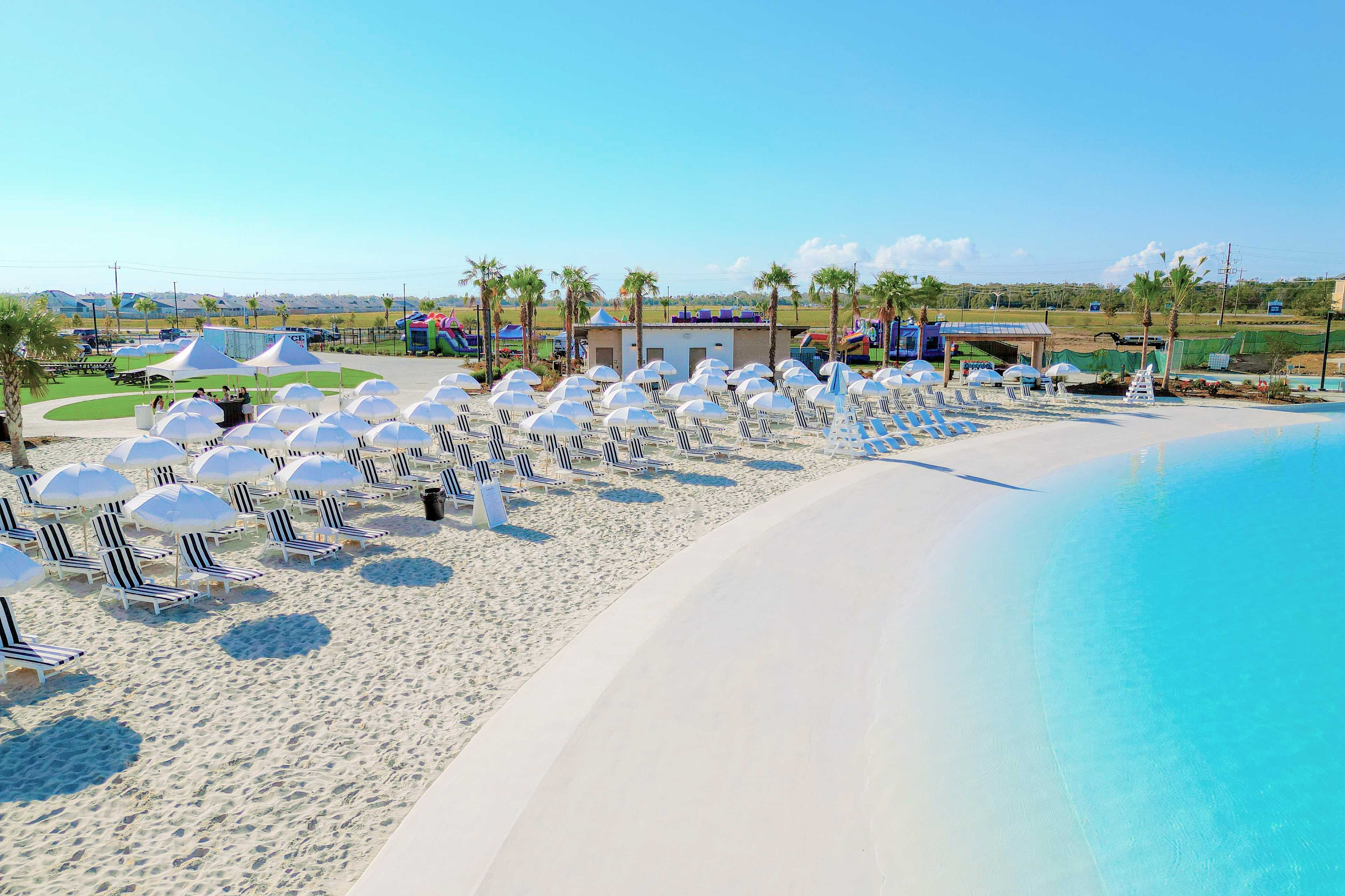 Resort-style beach-entry pool at River Ranch Meadows in Dayton TX with white sand, lounge chairs, umbrellas and palm trees