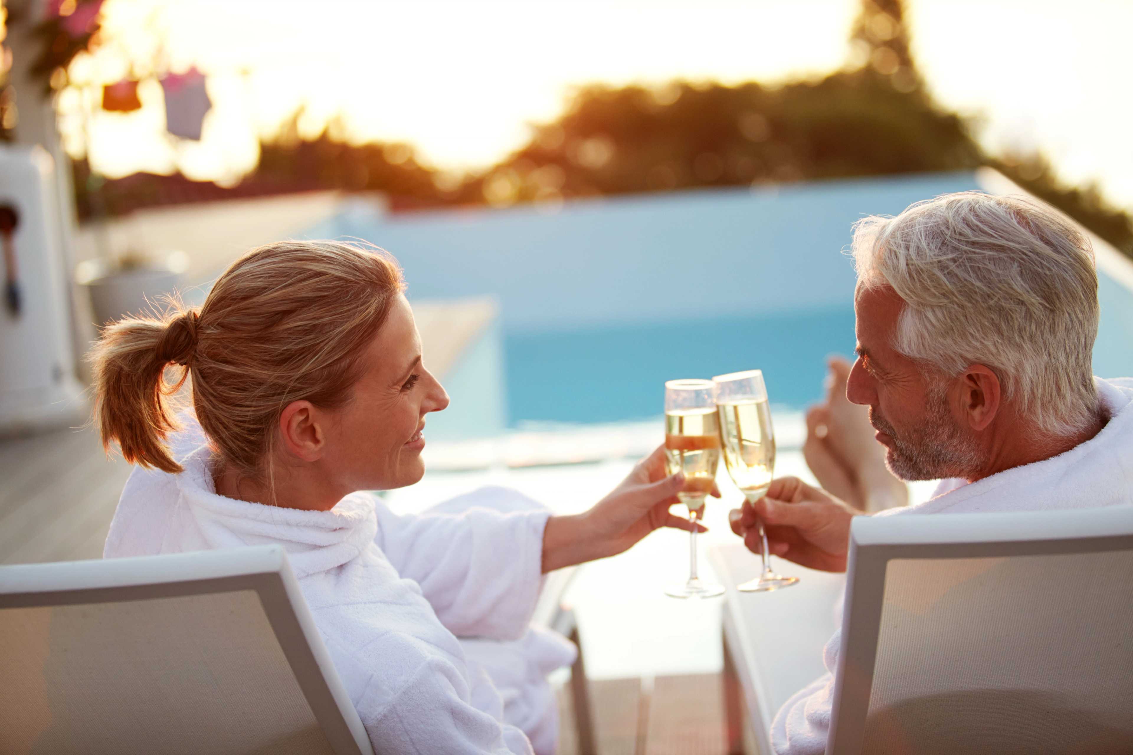Elderly couple in robes toasting champagne by infinity pool at sunset in Kelly Preserve, Loganville Georgia