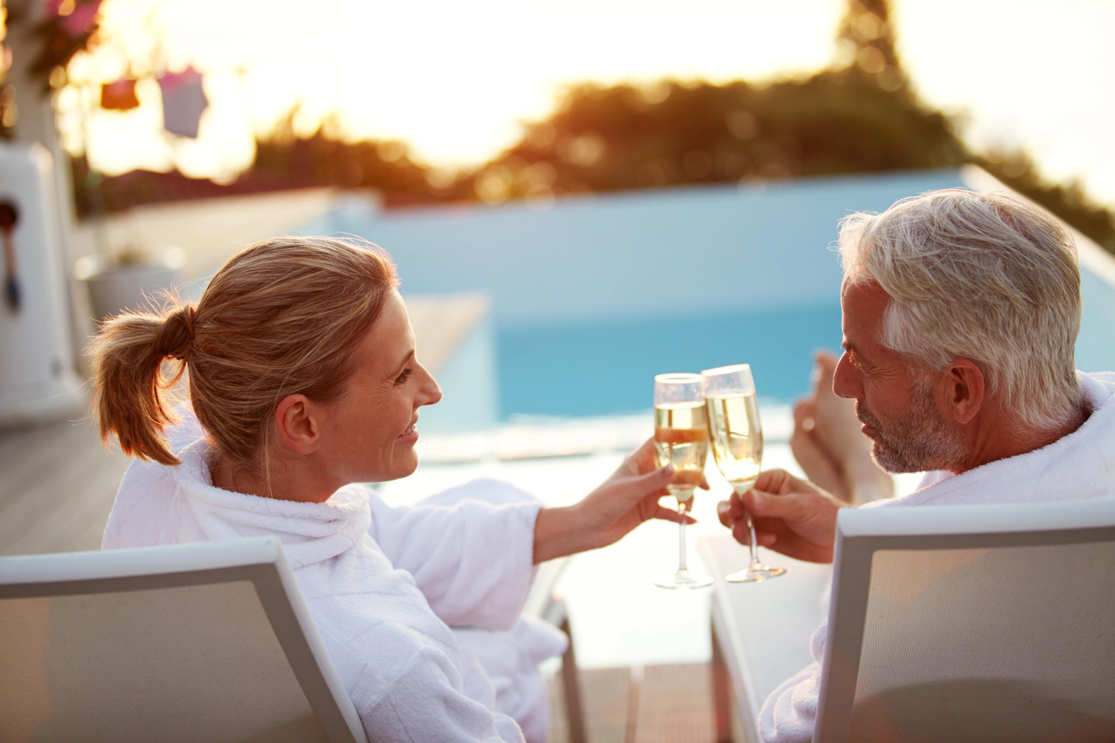 Elderly couple in robes toasting champagne by infinity pool at sunset in Kelly Preserve, Loganville Georgia