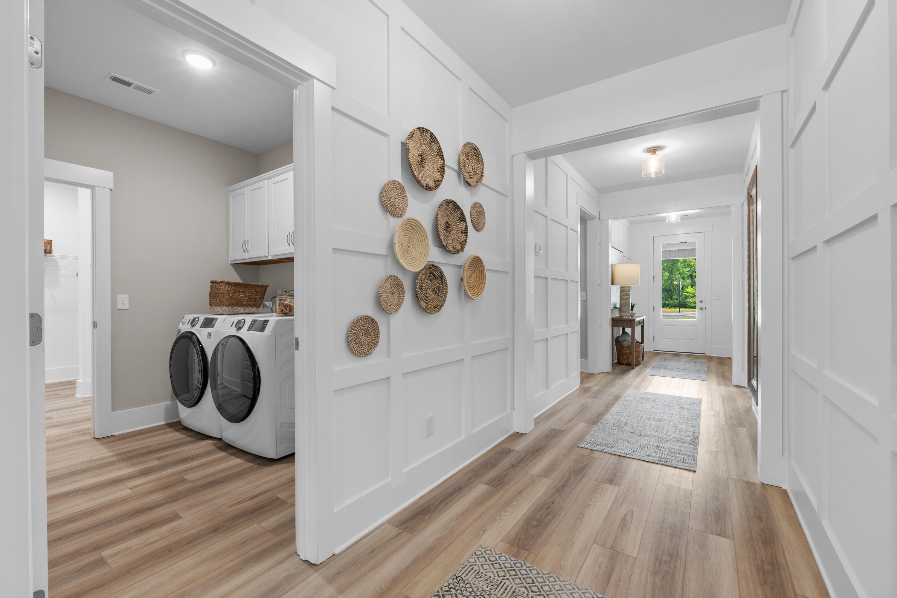 Spacious laundry room and hallway in The Highlands Arab Alabama home by Davidson Homes with white washer dryer wainscoting and woven wall decor