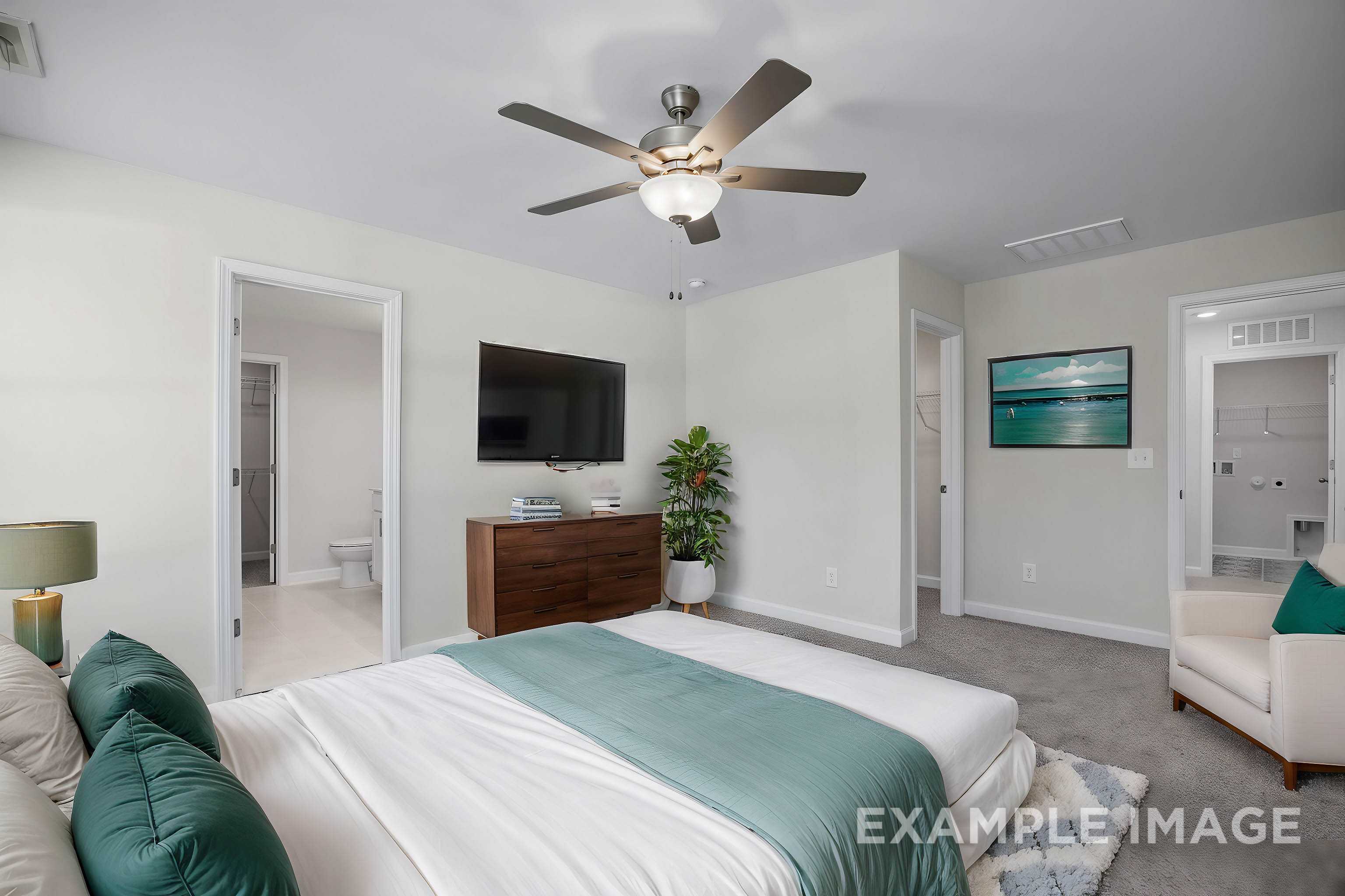 Spacious master bedroom in The Grace A with king bed, emerald pillows, wall TV, en-suite bath, and potted plant