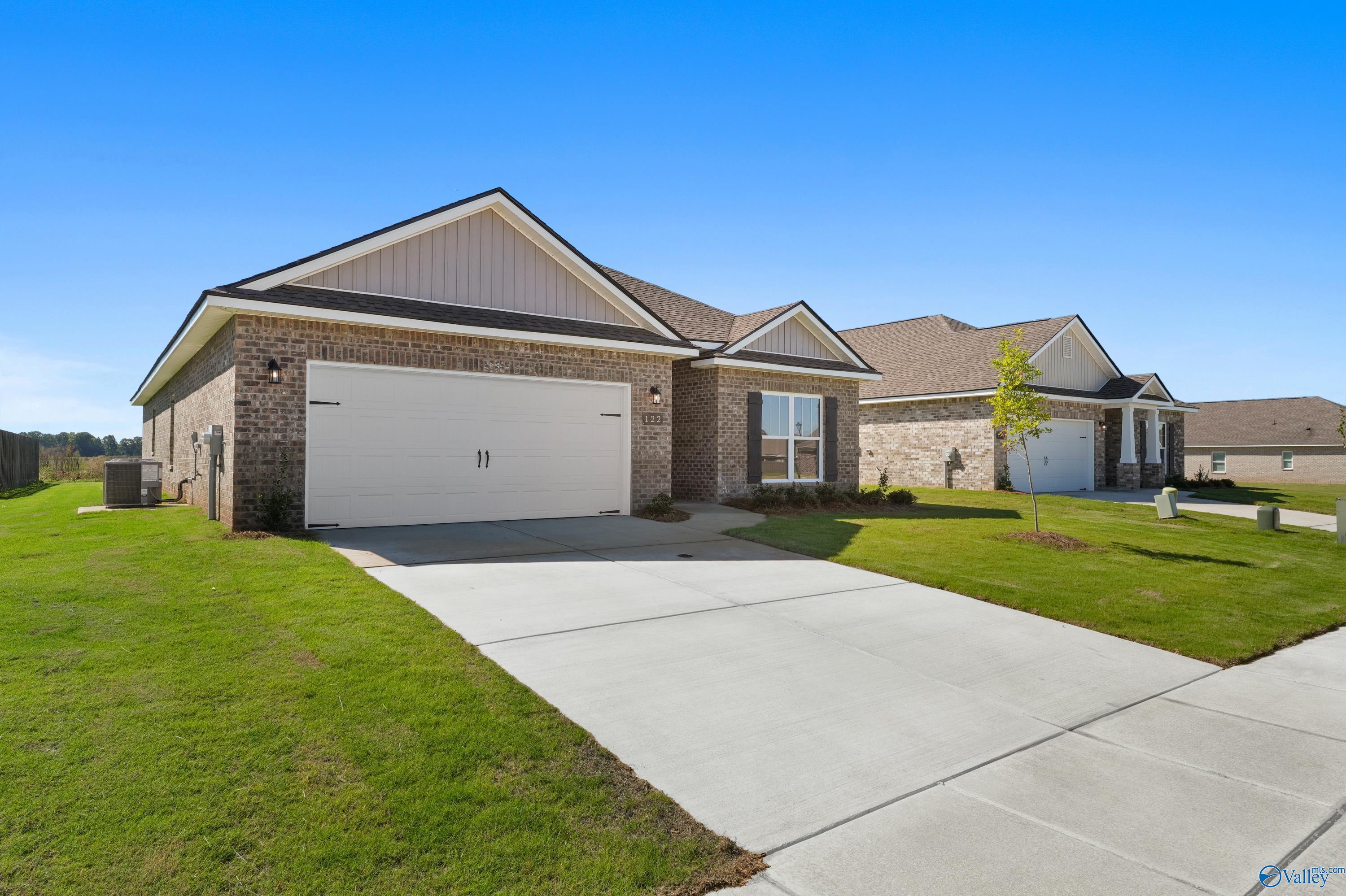 Modern tan brick 1-story home with 2-car garage, driveway, and lush green lawn in Clearview, Hazel Green, Alabama by Davidson Homes The Everett