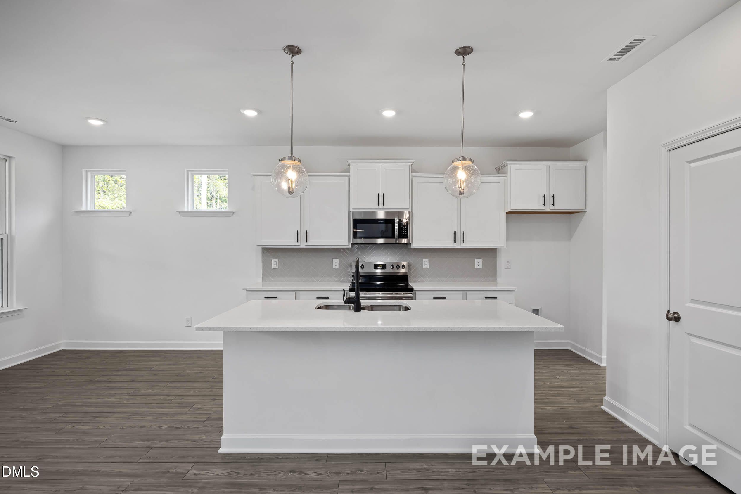 Bright modern kitchen with white island, cabinets, stainless appliances, and pendant lights in Davidson Homes Willow D, Zebulon, NC