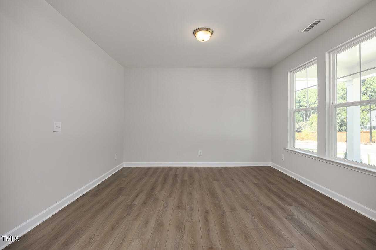 Spacious empty living room with light gray walls, hardwood floors, and large windows in Davidson Homes The Aspen C, Wake Forest, NC