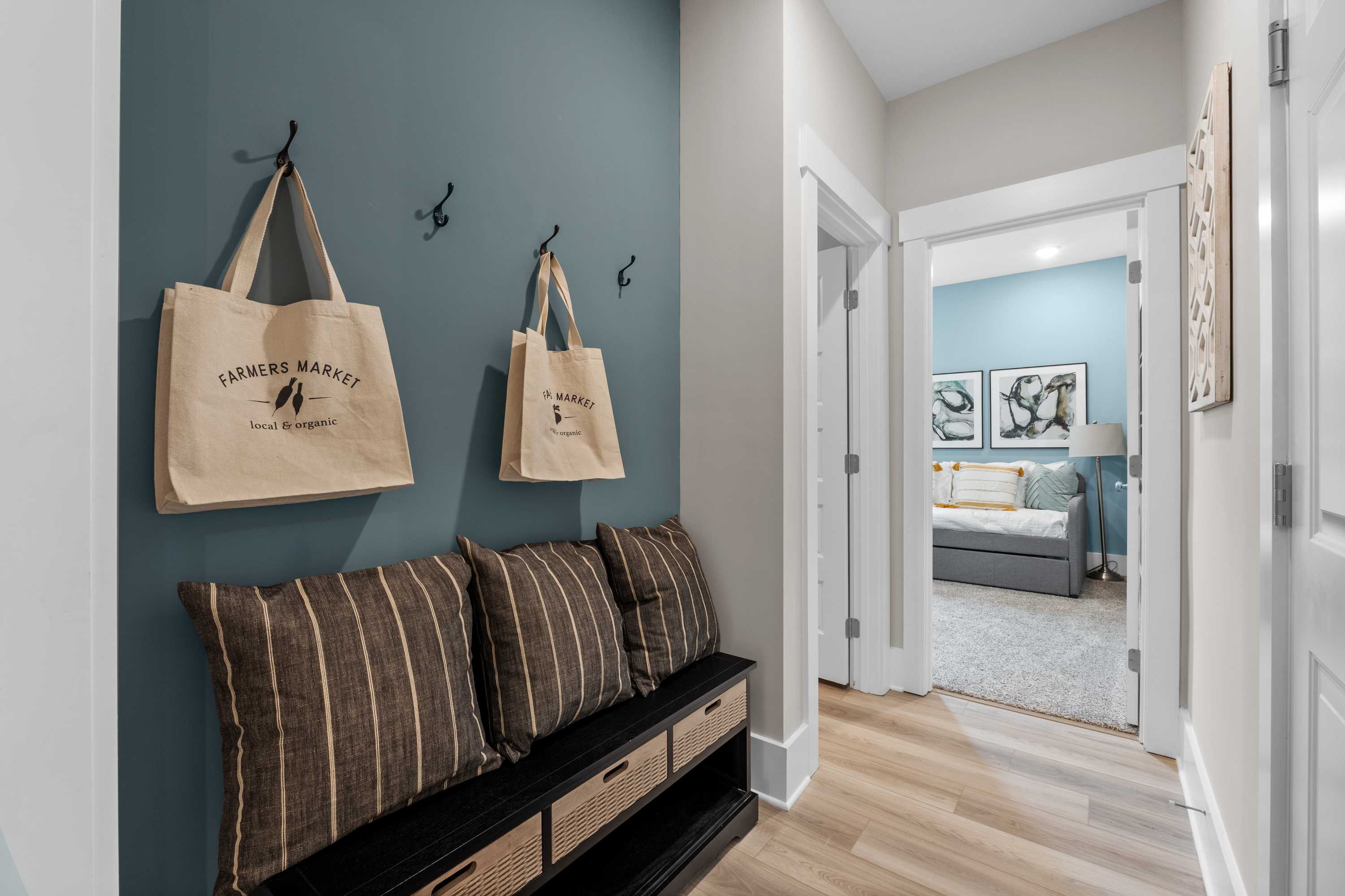 Stylish entryway with teal accent wall, Farmers Market tote bags on hooks, striped cushioned bench at The Highlands in Arab, Alabama