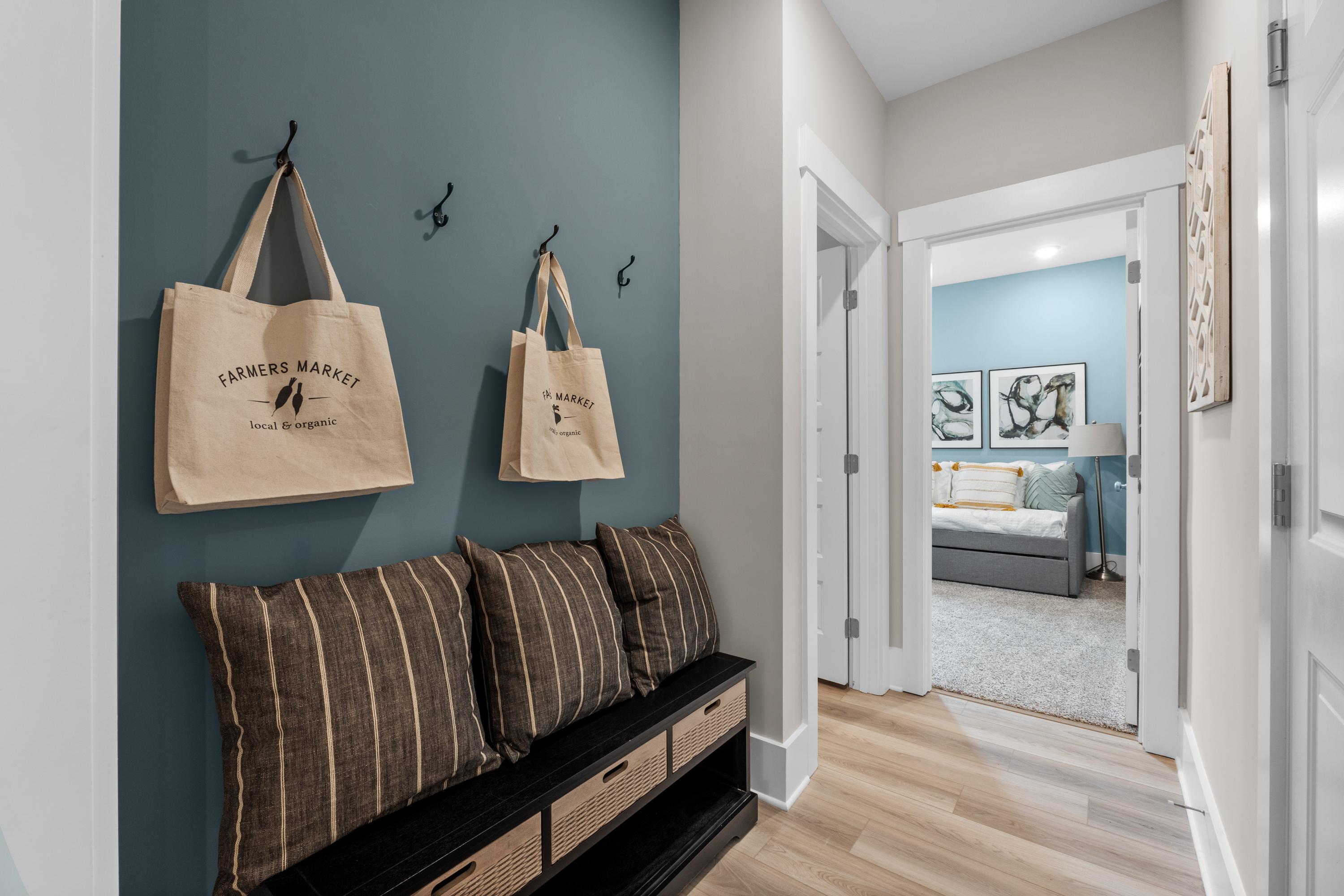 Stylish entryway with teal accent wall, Farmers Market tote bags on hooks, striped cushioned bench at The Highlands in Arab, Alabama