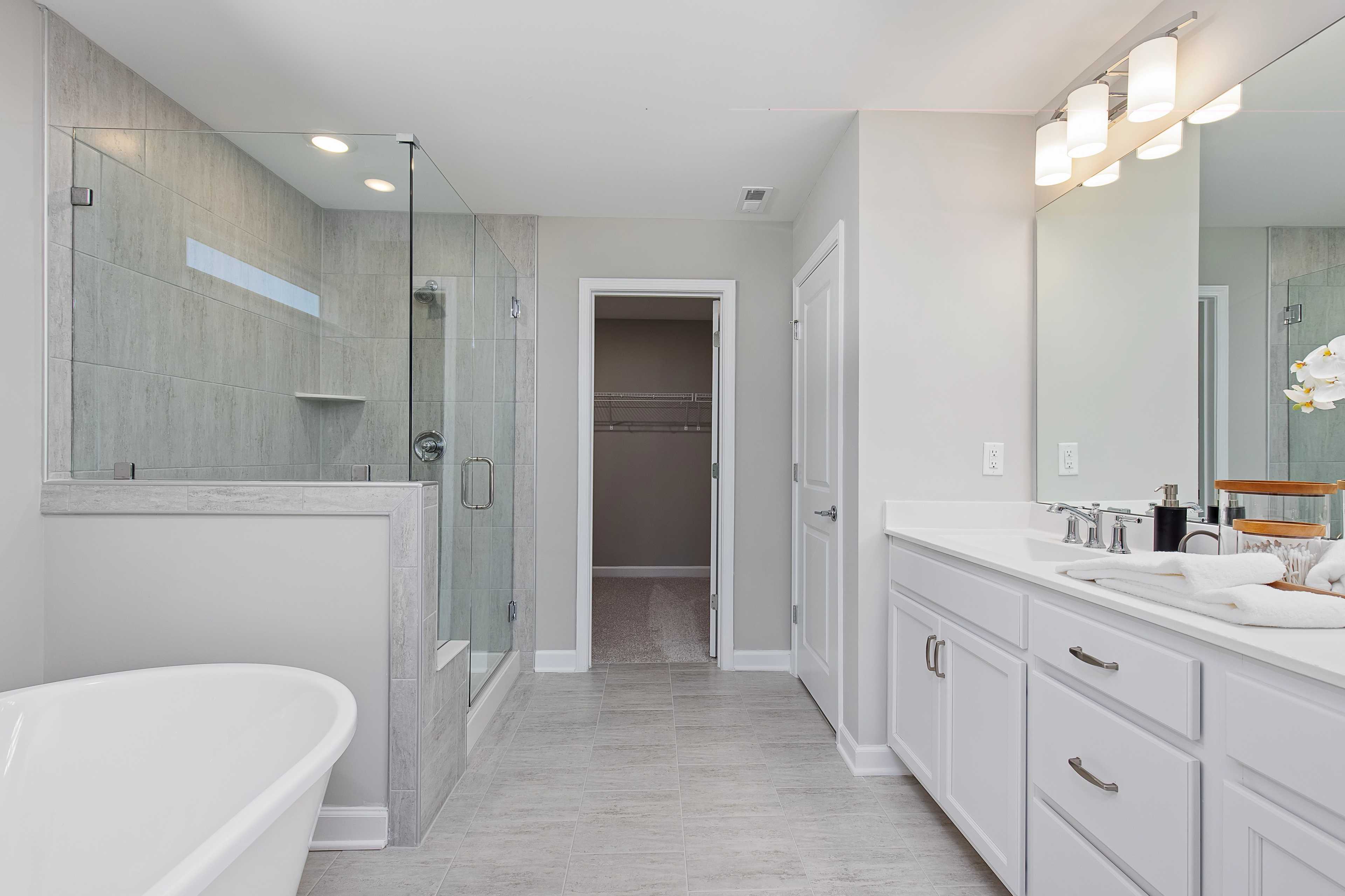 Spacious primary bathroom at Woodland Crossing in Zebulon NC with freestanding tub, glass shower, double vanity, and walk-in closet