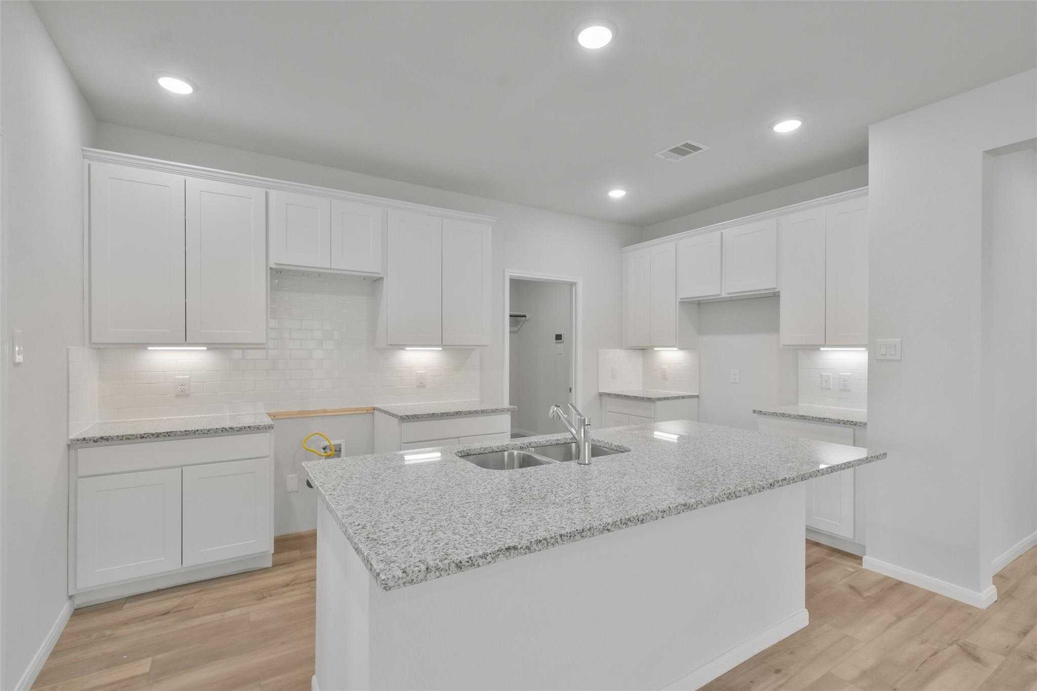 Modern white kitchen with granite island sink, subway tile backsplash, and hardwood floors in Davidson Homes The Tierra A, Dayton, Texas