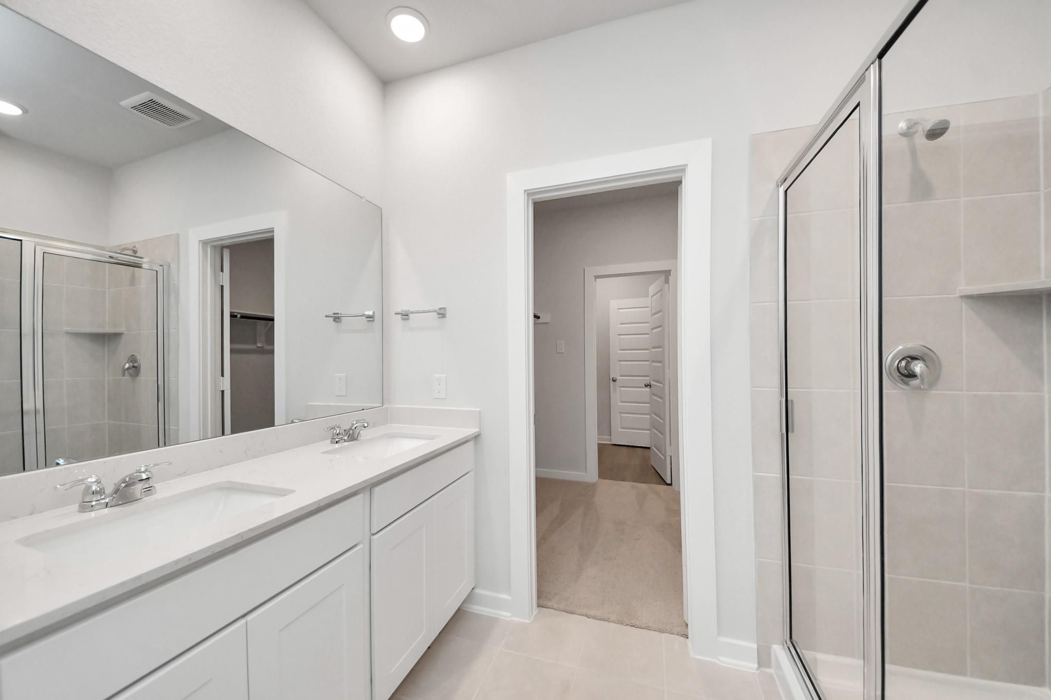 Modern primary bathroom with double vanity and walk-in shower in The Blanco E at Caney Creek Place, Conroe, Texas.