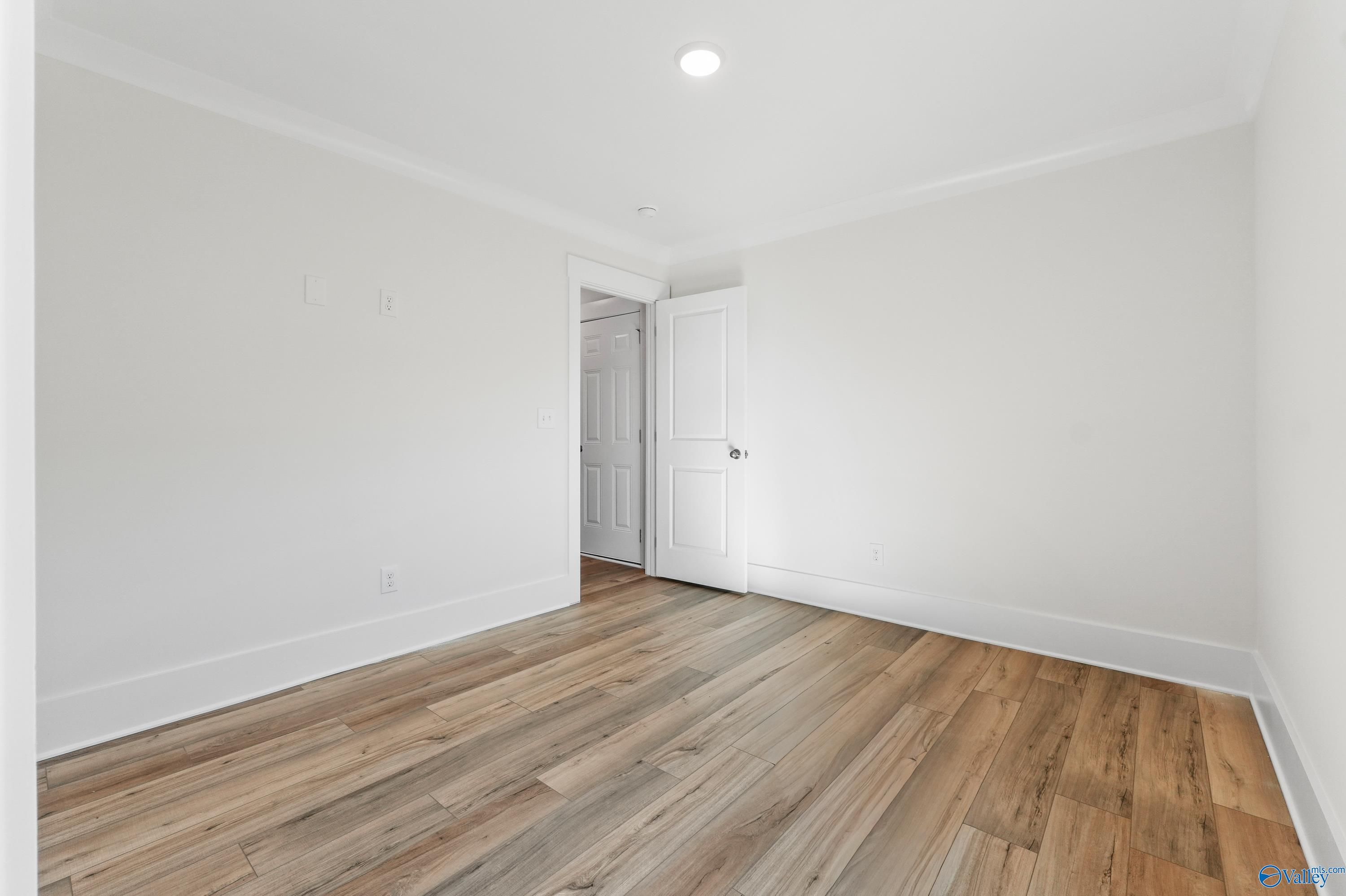 Bright secondary bedroom with light hardwood floors, white walls, and bathroom door in Davidson Homes The Daphne C, Arab, Alabama