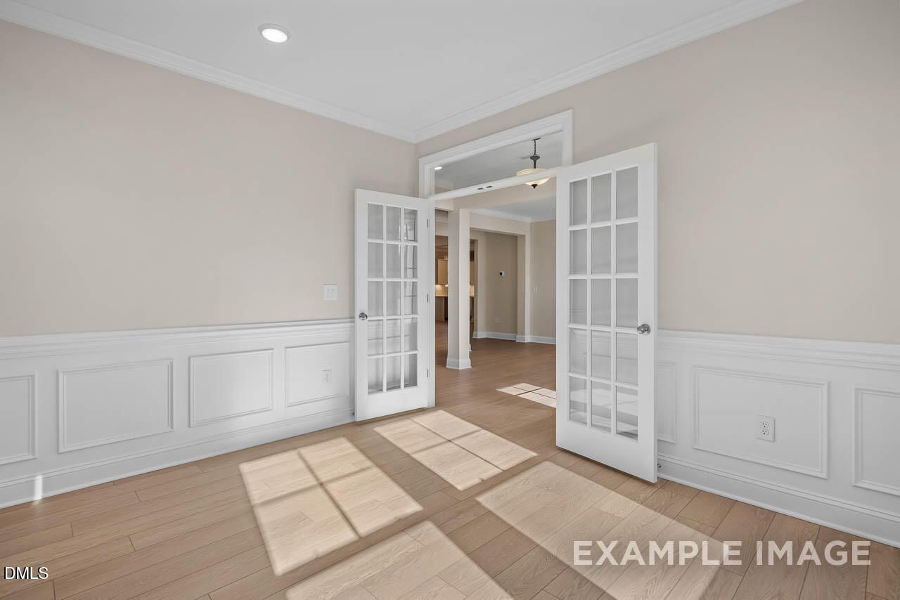 Bright formal room with open French doors, wainscoting, beige walls, and sunlit hardwood floors in Davidson Homes Crawford D, Angier NC