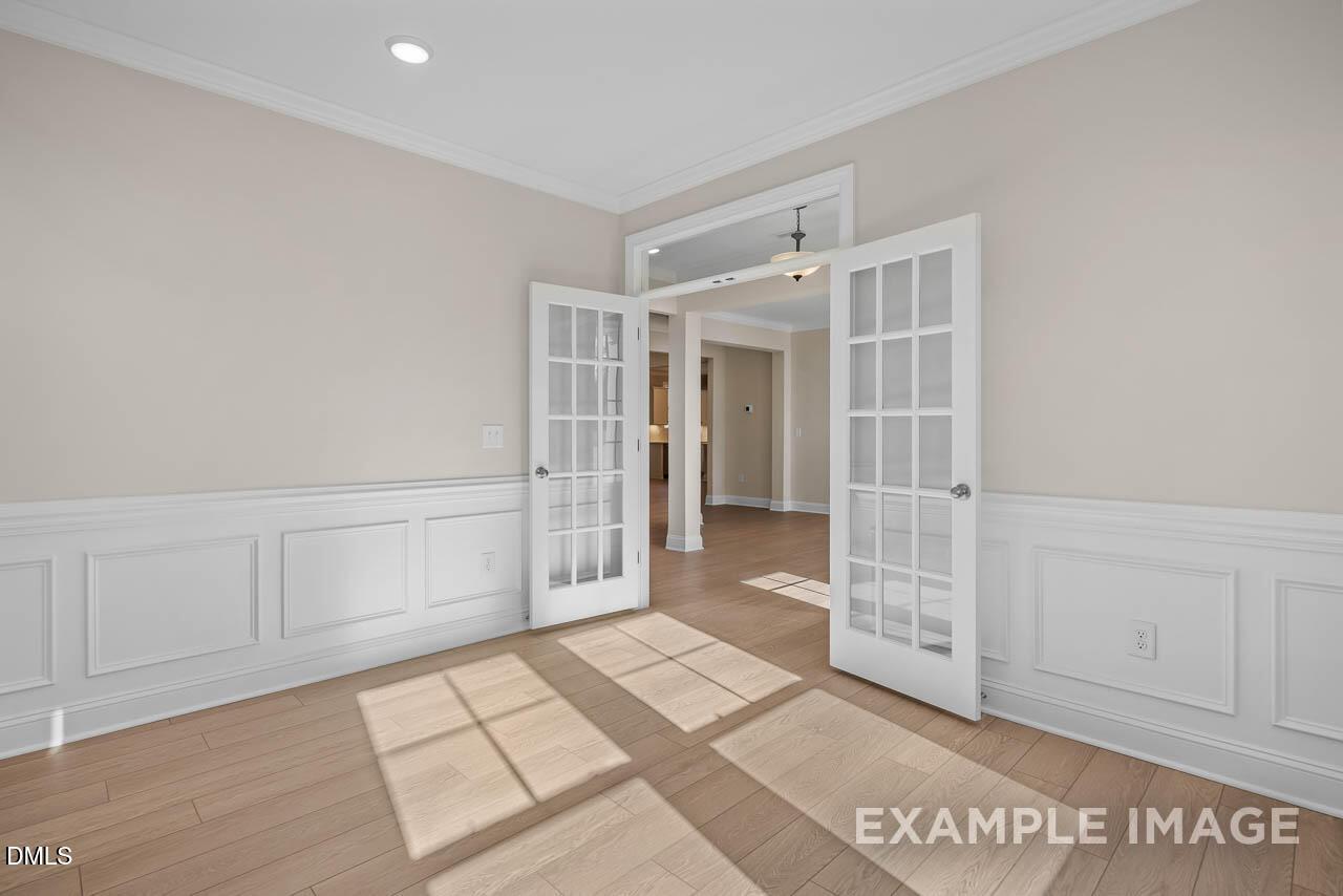 Bright formal room with open French doors, wainscoting, beige walls, and sunlit hardwood floors in Davidson Homes Crawford D, Angier NC