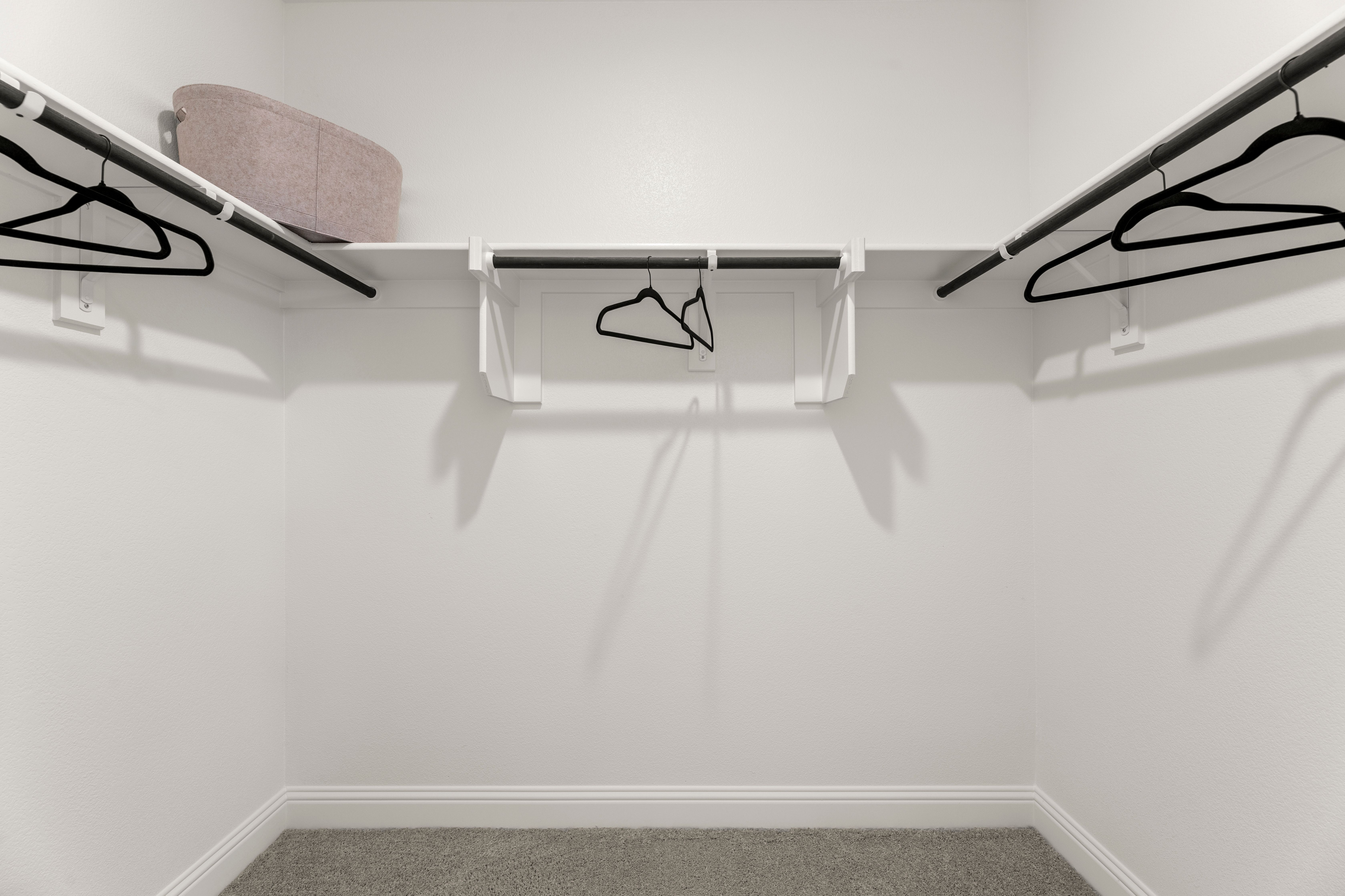 Spacious walk-in master closet in The Laurel by Davidson Homes with built-in shelves, hanging rods, white walls, neutral carpet