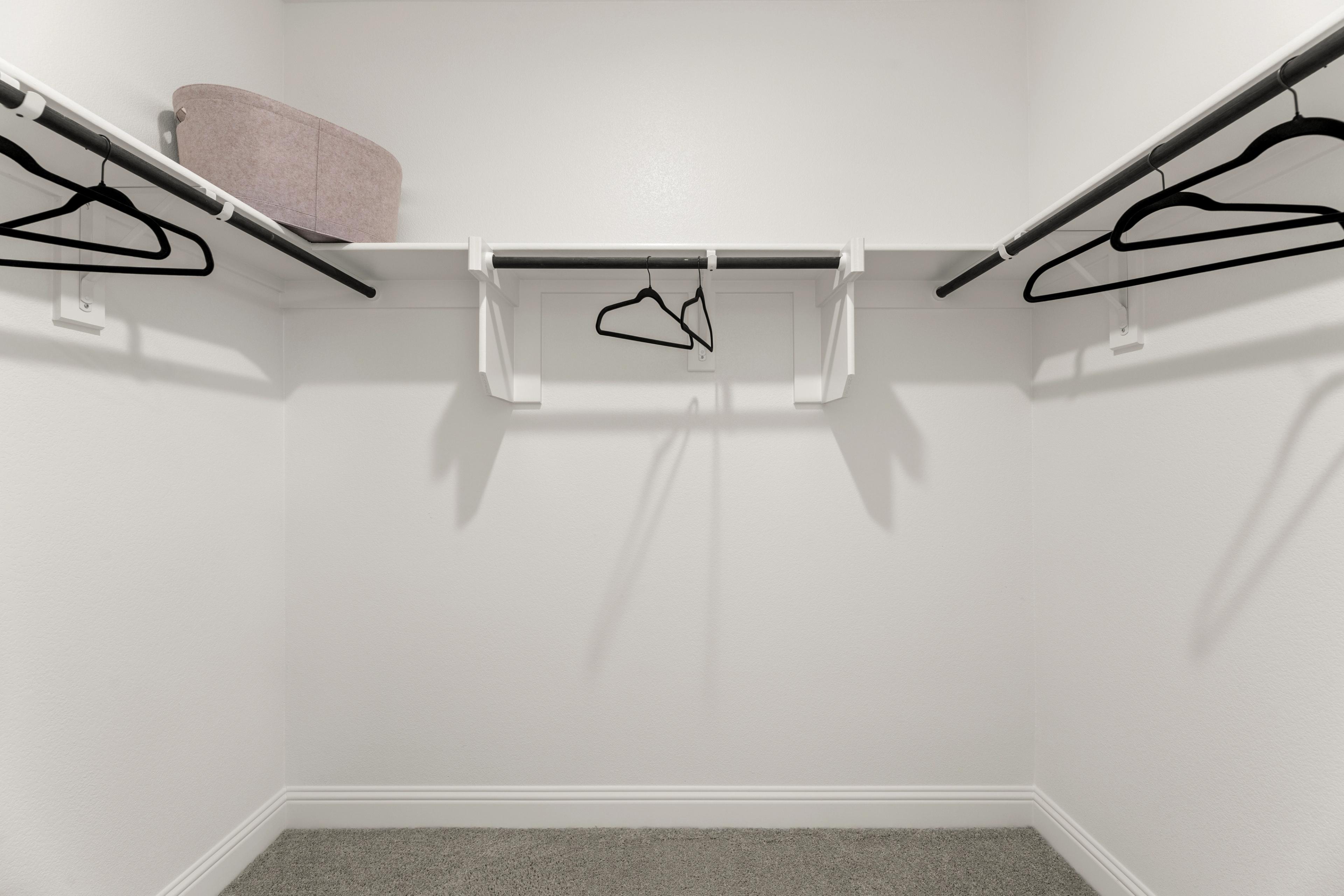 Spacious walk-in closet in The Laurel G master suite with wooden shelves, hanging rods, and gray carpet