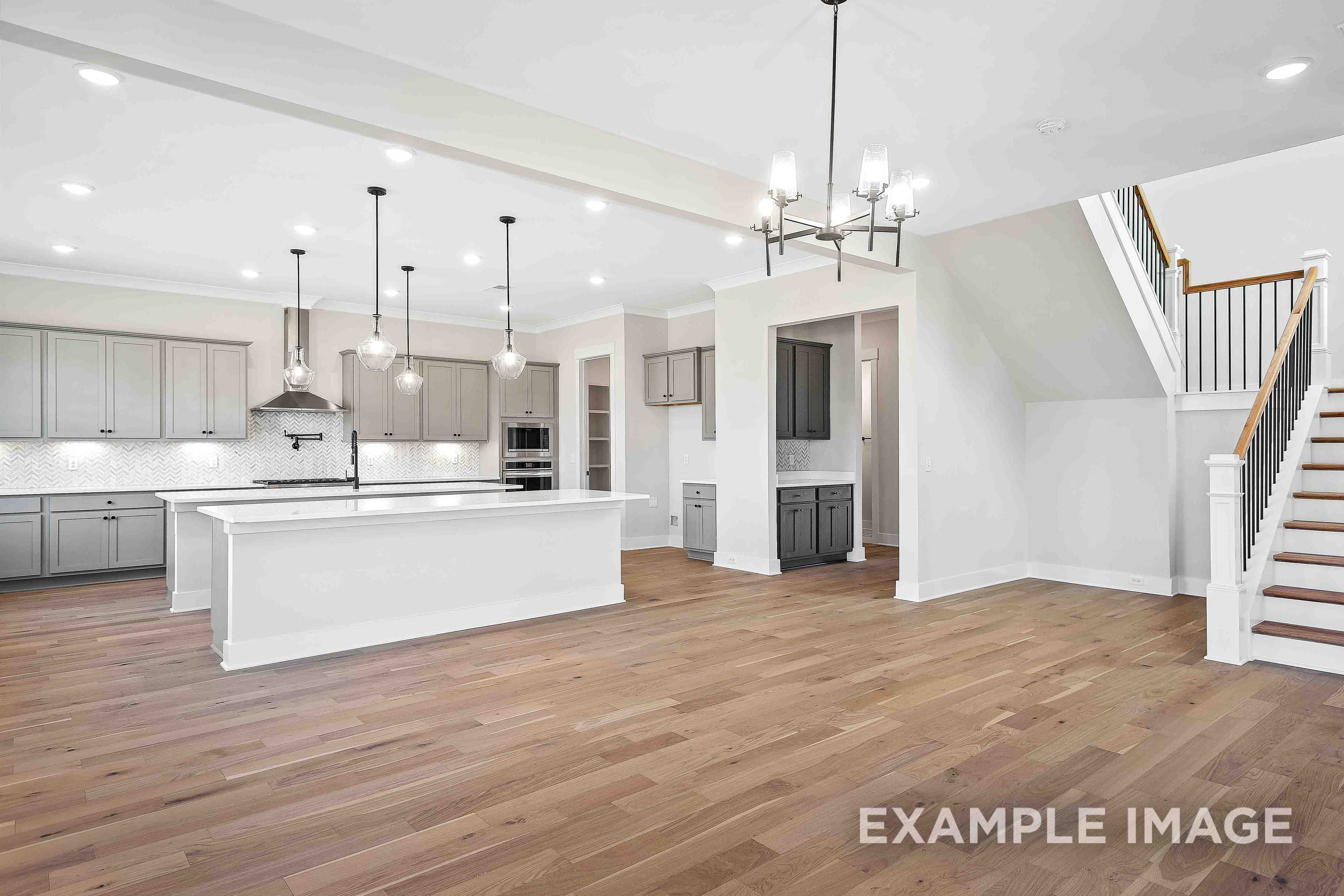 Spacious open-concept kitchen in The Alston A Davidson Homes design, white shaker cabinets, large island, stainless appliances, hardwood floors, staircase
