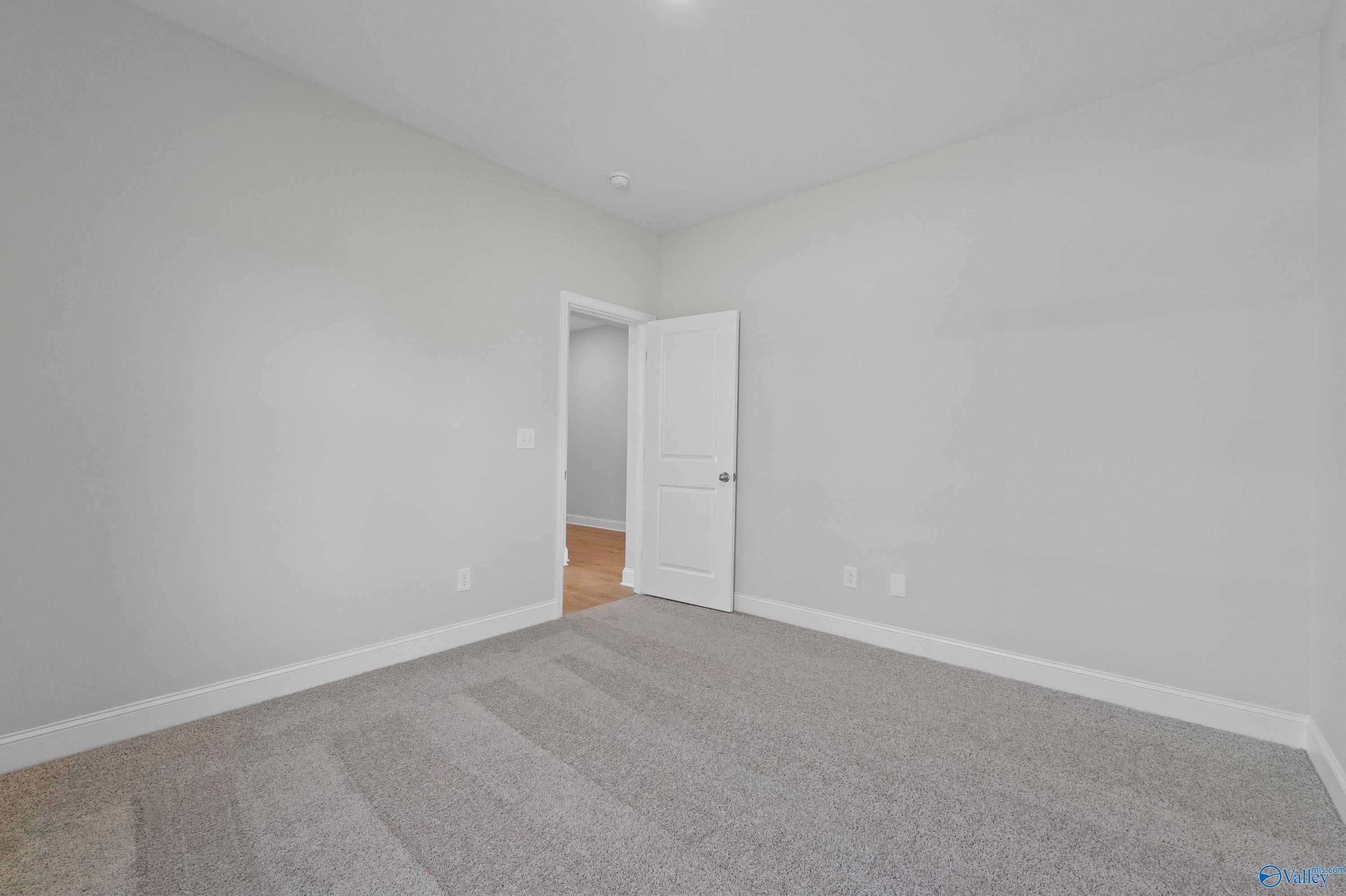 Spacious empty bedroom with light gray walls, beige carpet, and open door in Davidson Homes The Everett, Hazel Green, AL