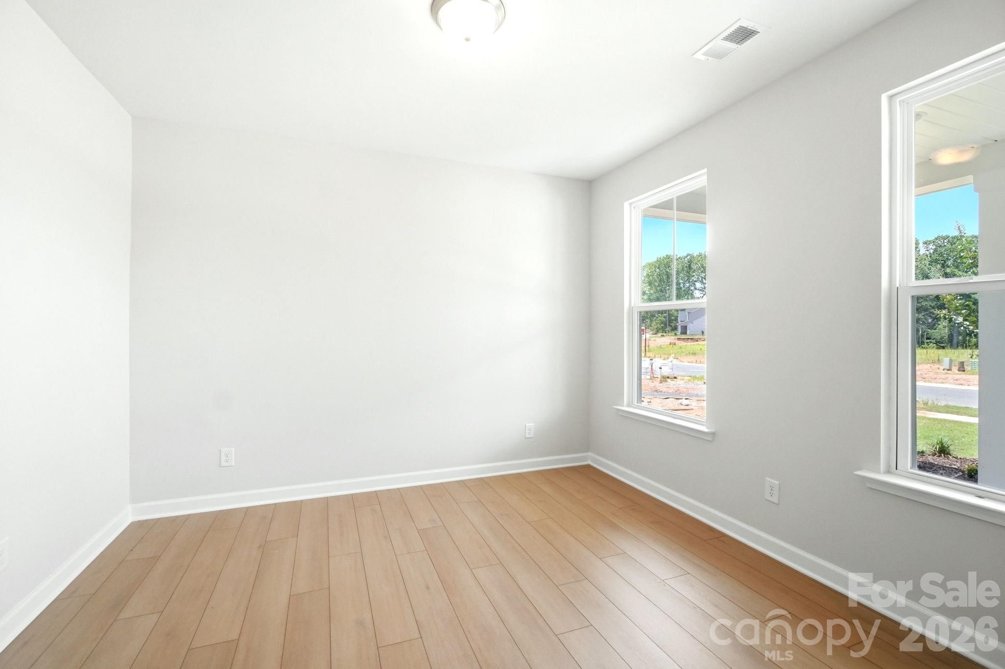 Bright, empty bedroom with light wood floors and large windows in The Magnolia B floor plan at Windgate, Mooresville, NC.