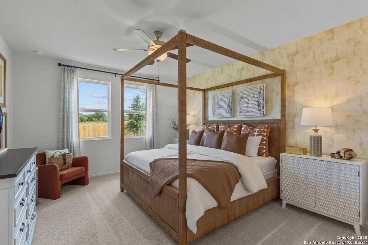 Elegant master bedroom with wooden canopy bed, neutral tones, and backyard view in Davidson Homes The Daphne J, Elmendorf, Texas
