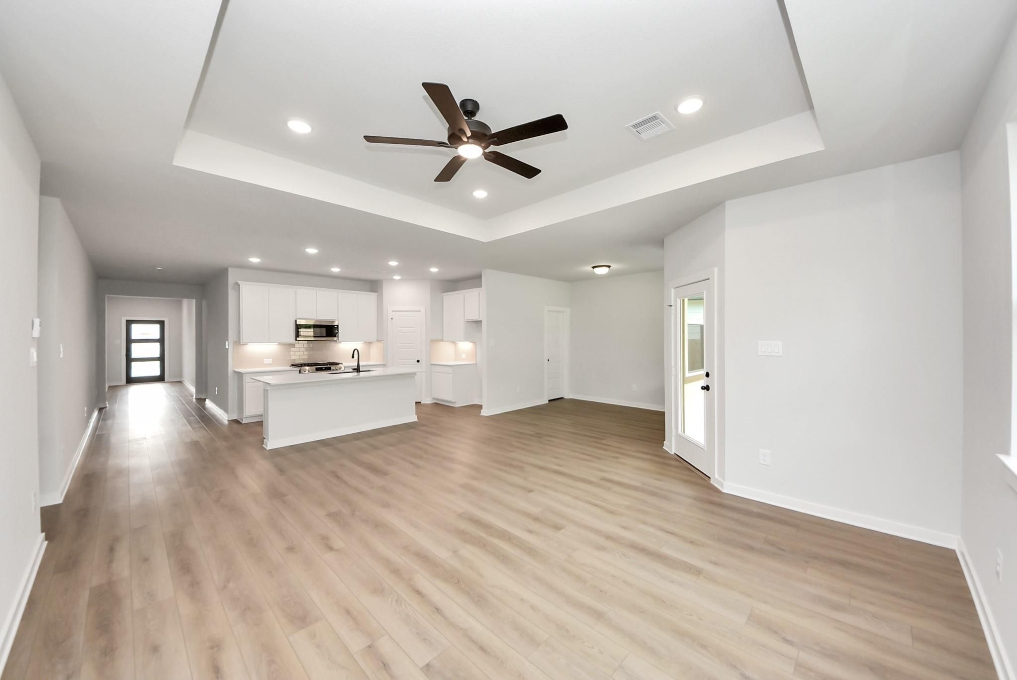 Open-concept living room and kitchen with tray ceiling in The Daphne F floor plan at Sundance Cove, Crosby, Texas.