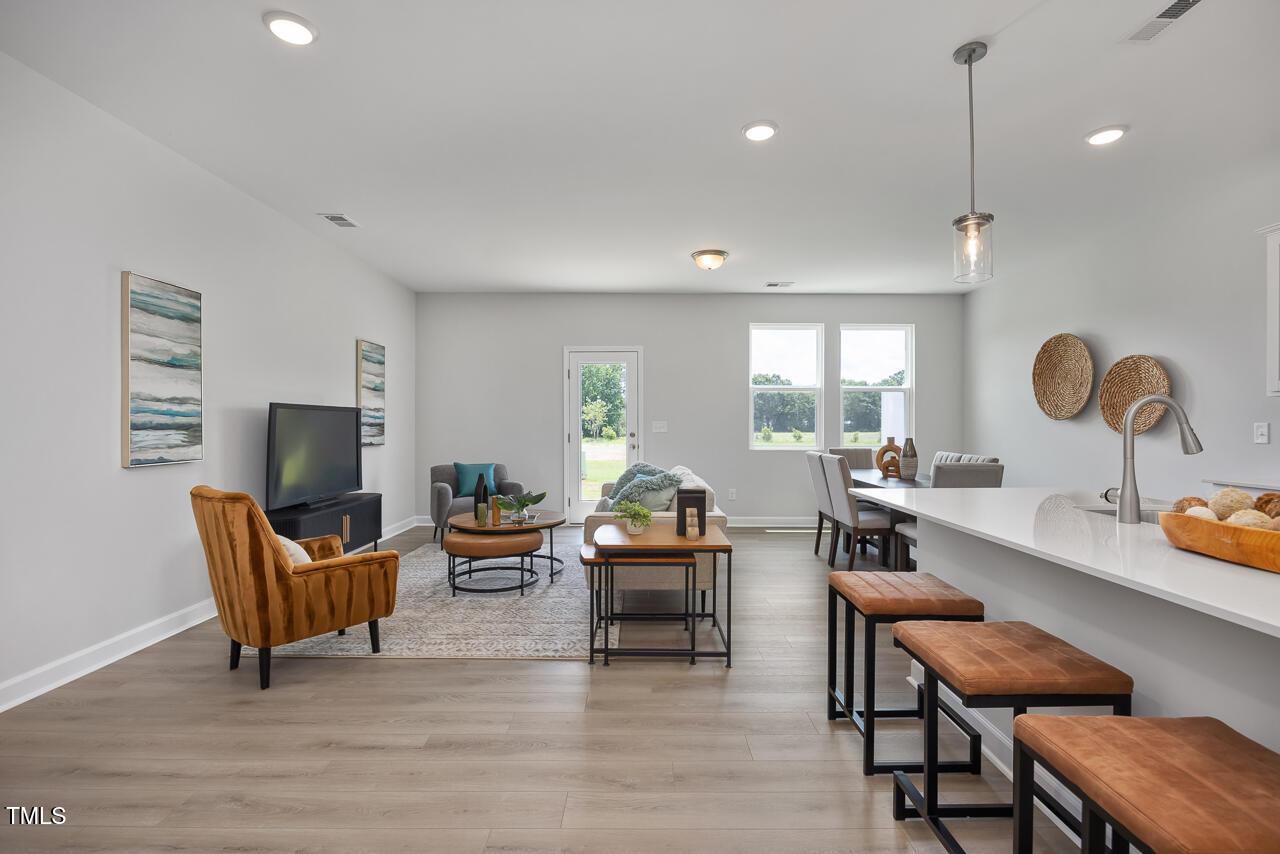 Open-concept living-dining-kitchen with mounted TV, orange armchair, wood island stools, and sink in Davidson Homes The Warren plan, Fuquay-Varina, NC