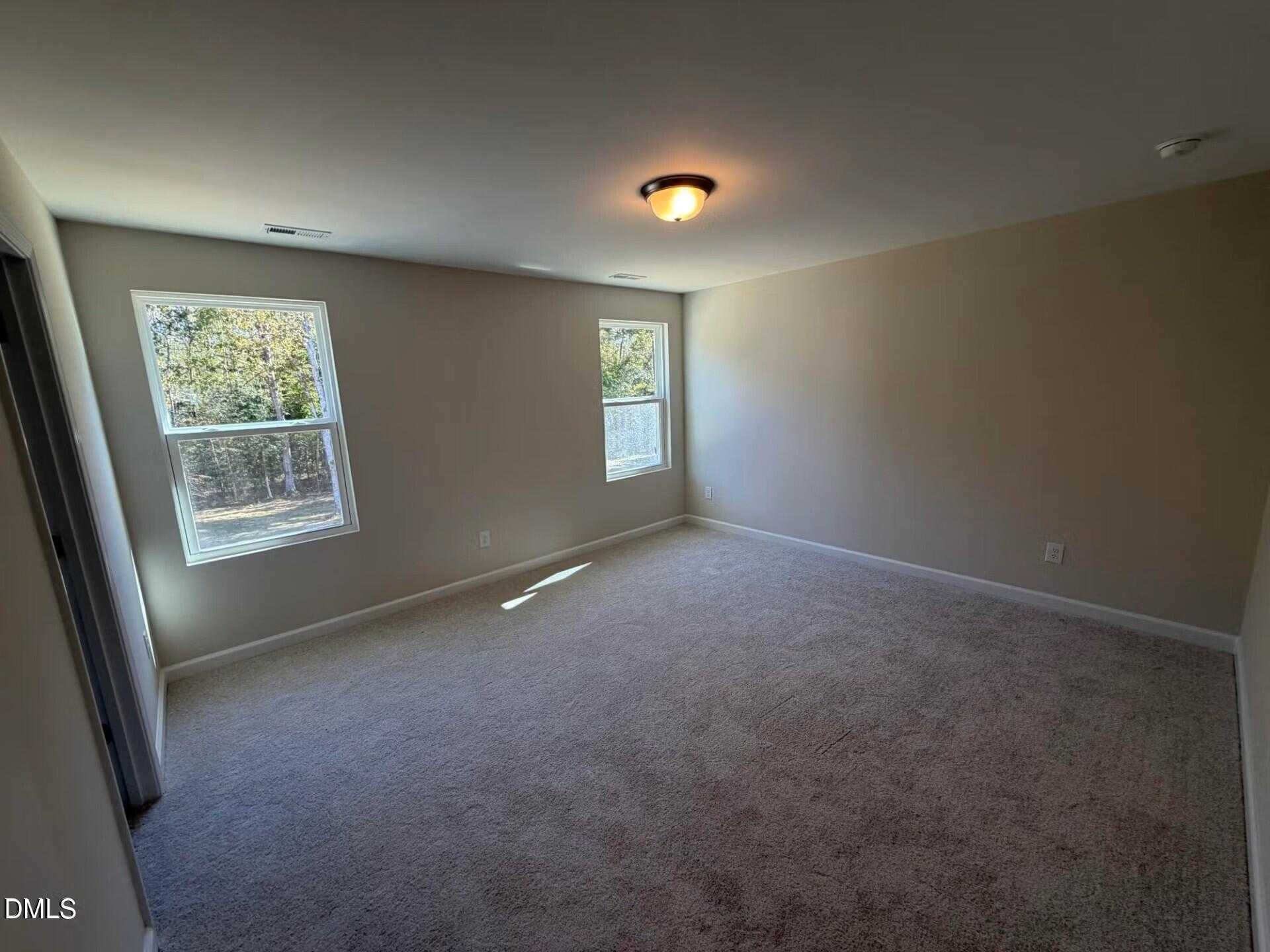Spacious empty bedroom with beige walls, neutral carpet, large windows overlooking trees in Davidson Homes The Gavin C, Lillington, NC