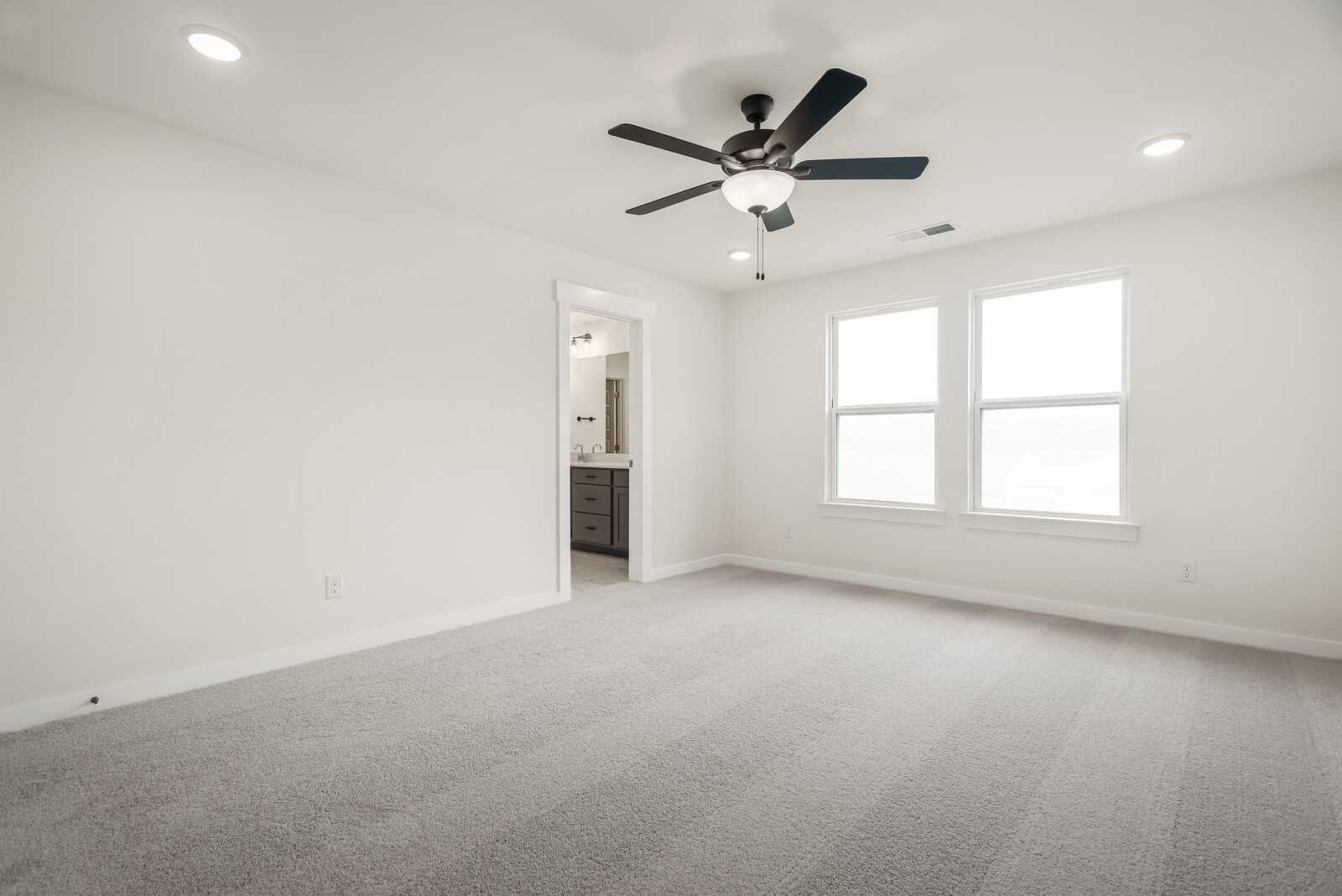 Spacious master bedroom with ceiling fan, en-suite bath vanity, and double windows in Davidson Homes The Logan C, Gallatin, TN