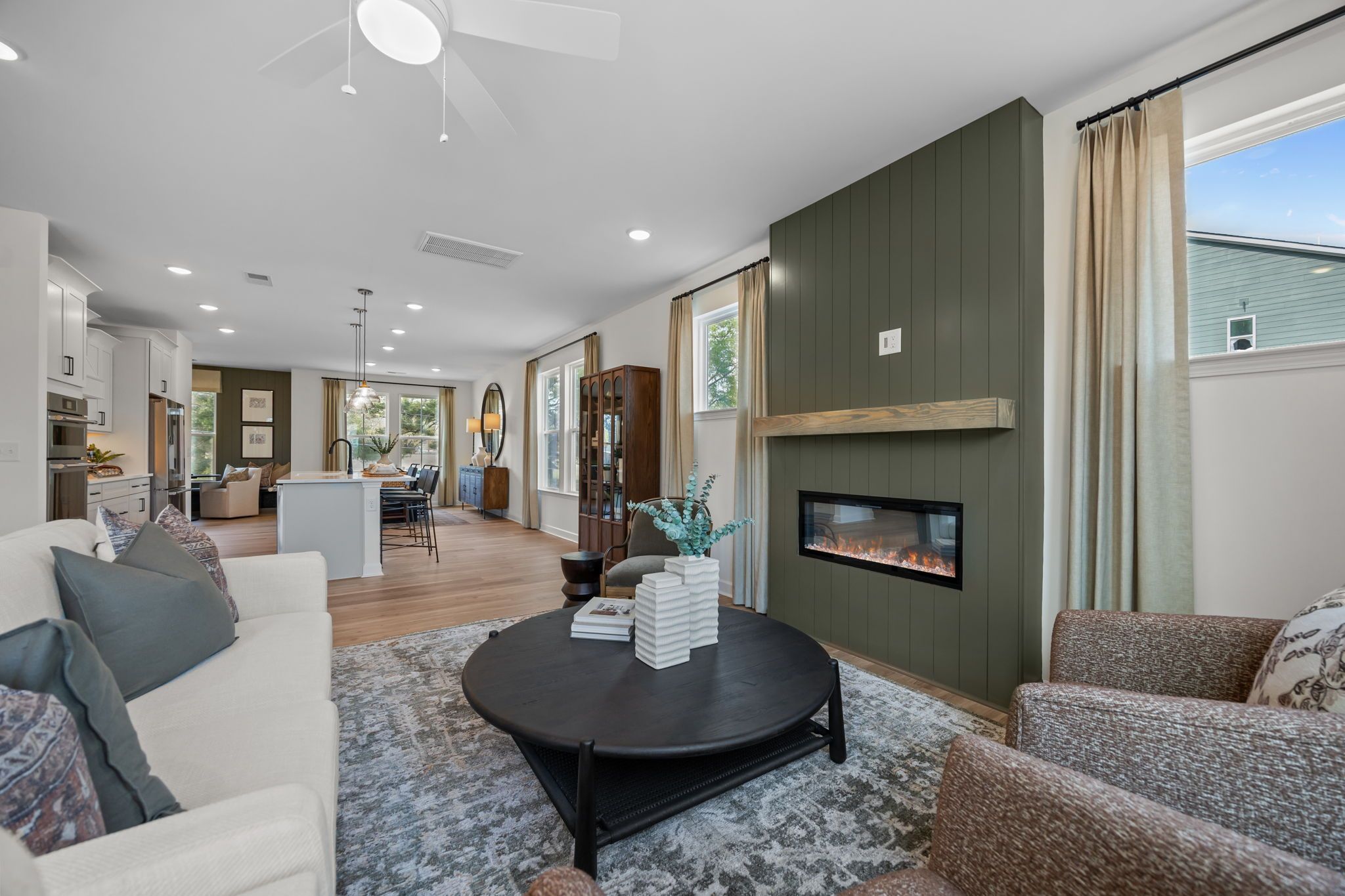 Spacious open-concept living room in Camden Park Knightdale NC with green accent wall, linear gas fireplace, hardwood floors