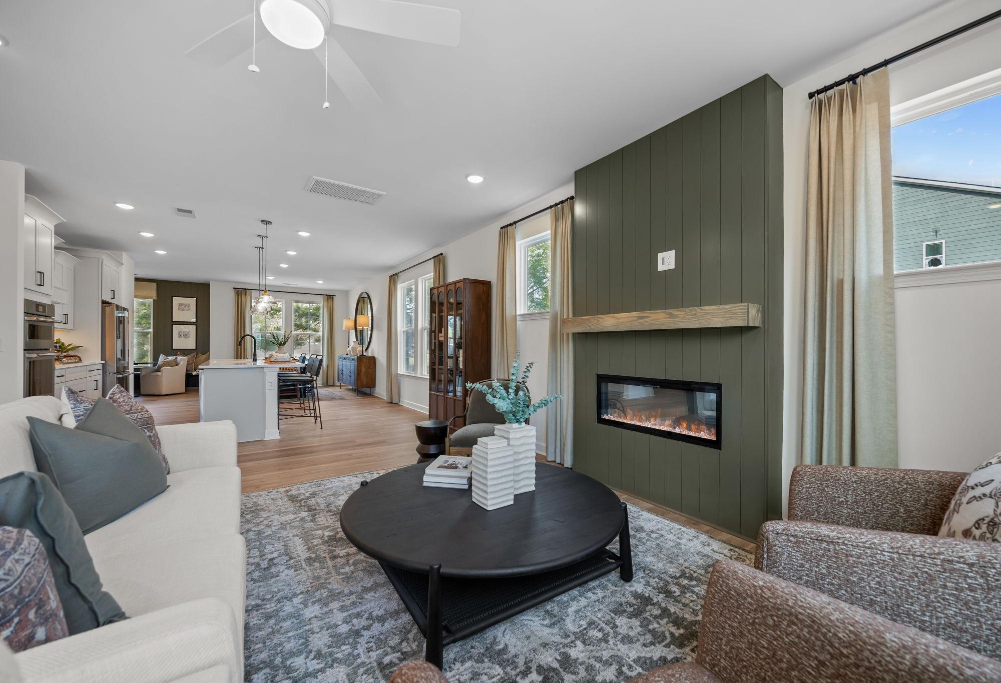 Open-concept living room in The Mitchell featuring a modern fireplace with green accent wall and spacious kitchen island.