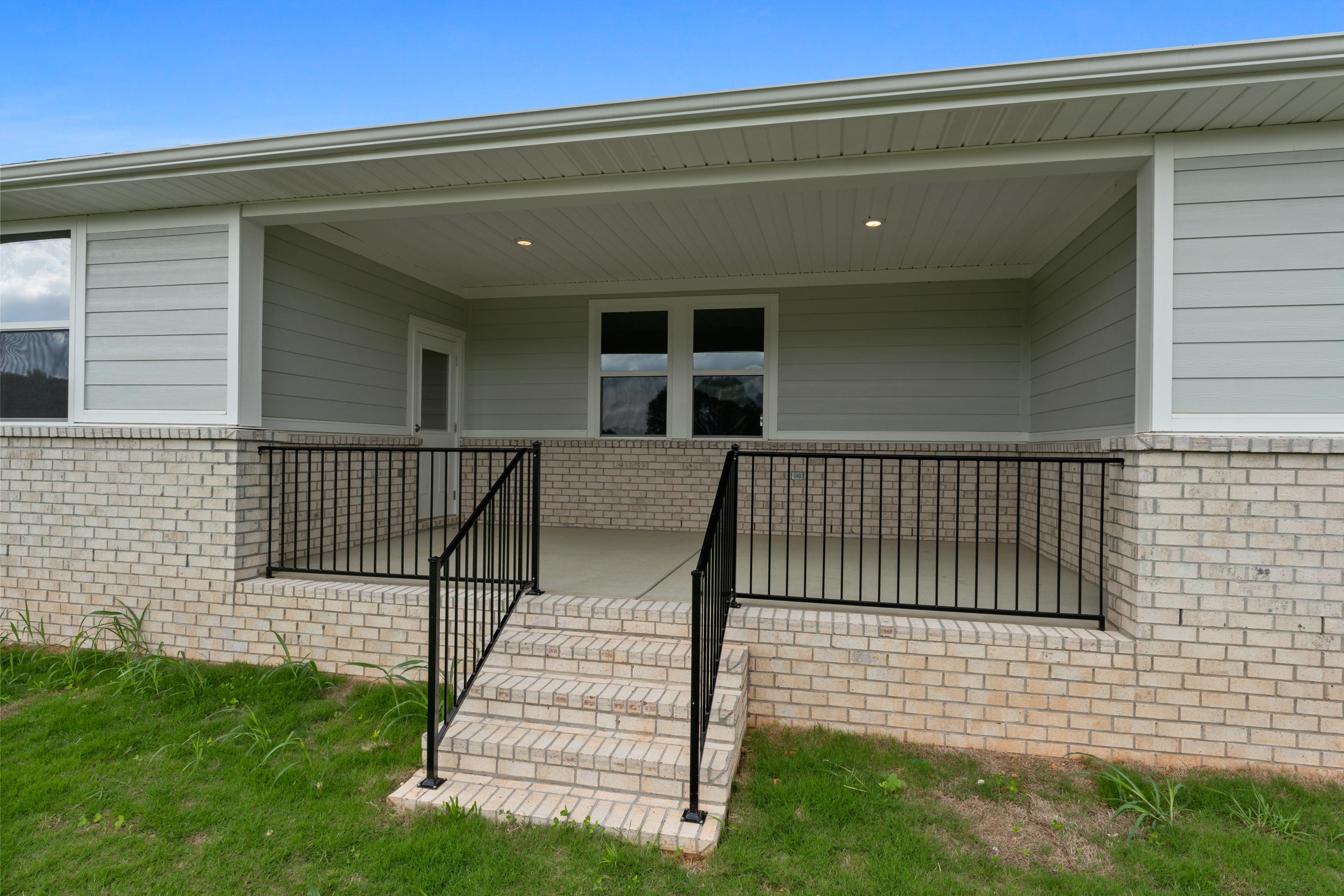Covered porch of The Haven E home design featuring black metal railing, brick steps, and large windows overlooking lawn