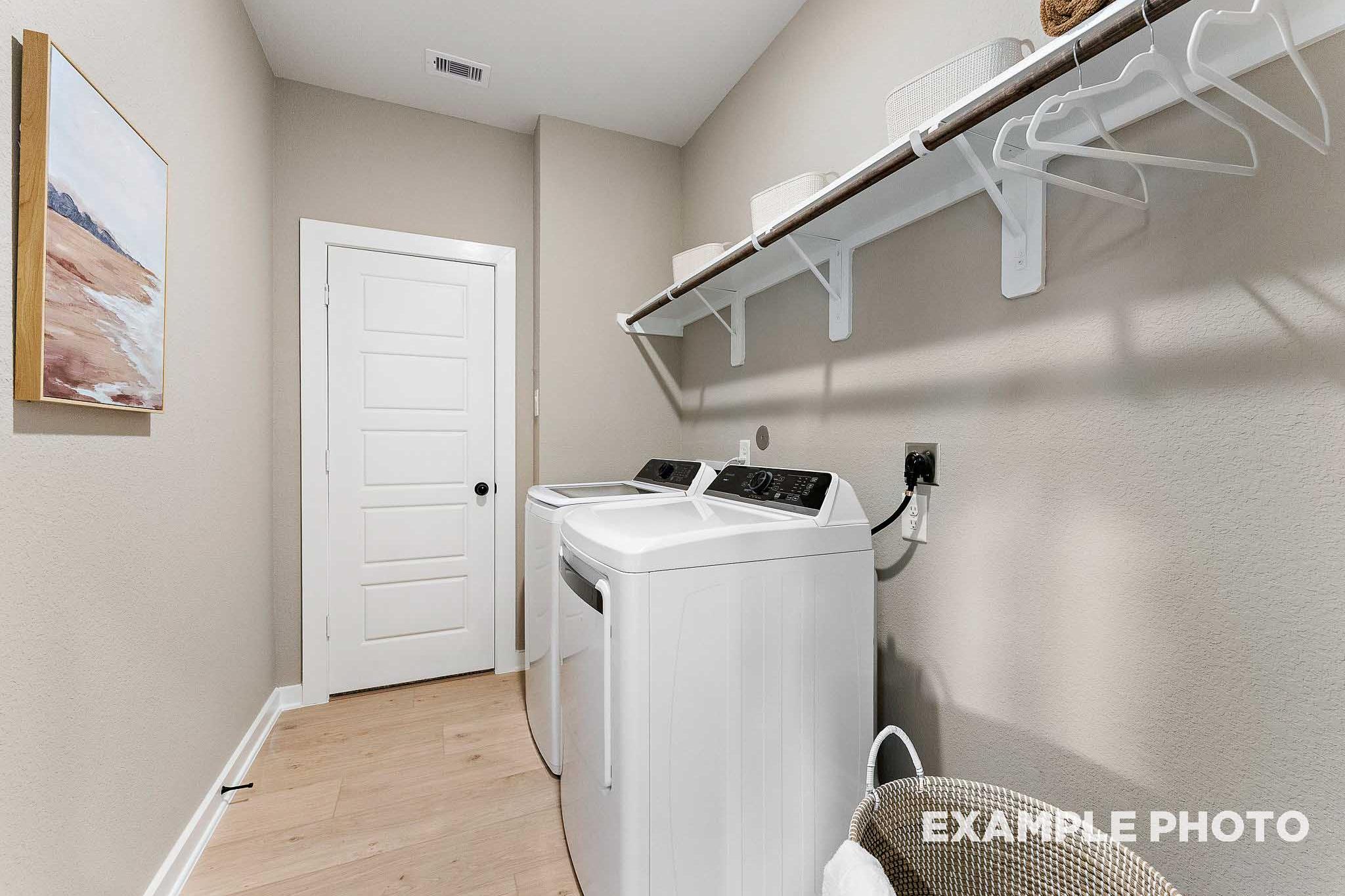 Spacious laundry room in The Everett E featuring white washer dryer, built-in wooden shelves, beige walls, and hardwood floors by Davidson Homes