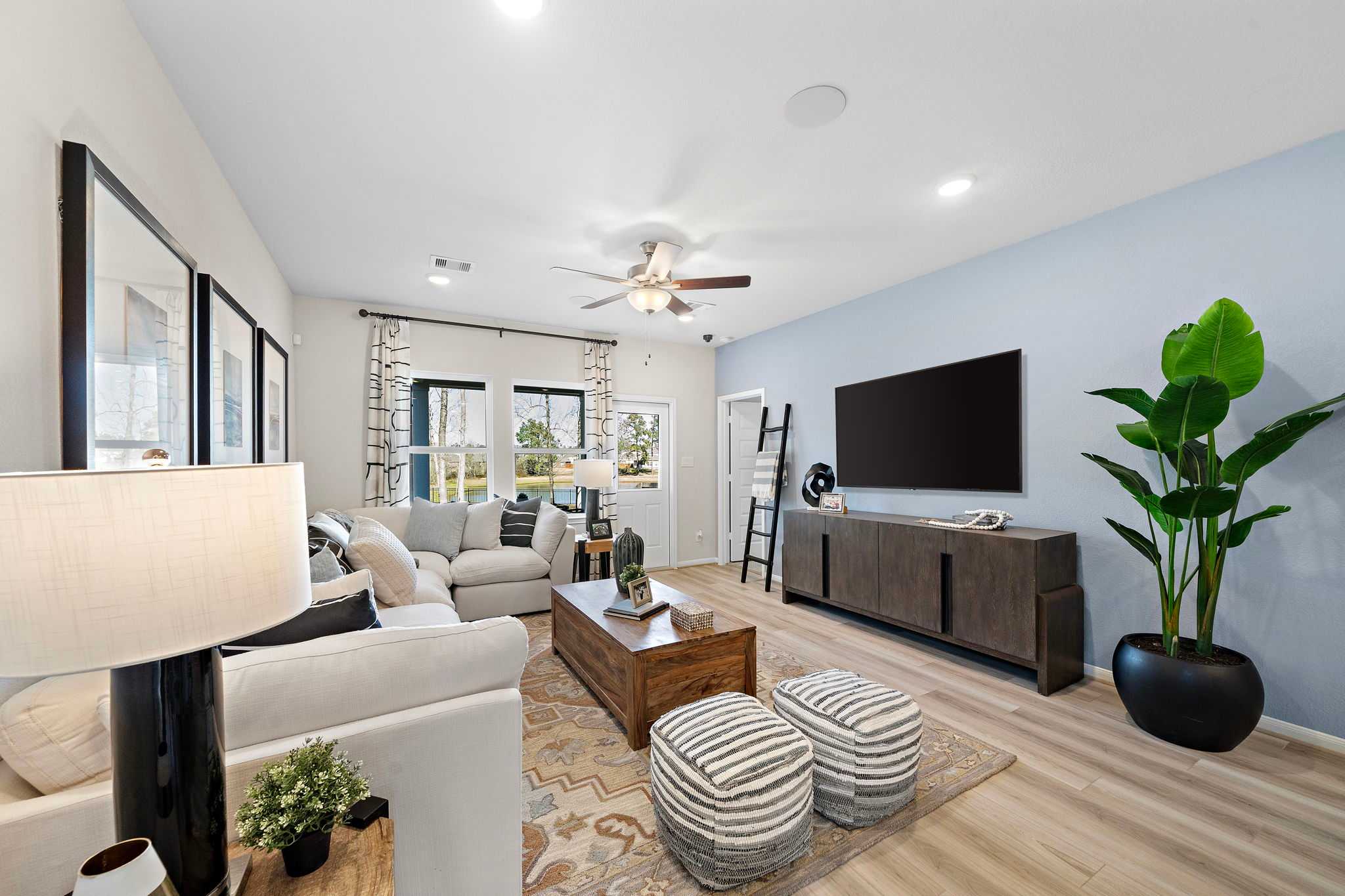 Open-concept living room at Lakes at Black Oak in Magnolia TX with white sectional sofa, hardwood floors, ceiling fan, and potted plant
