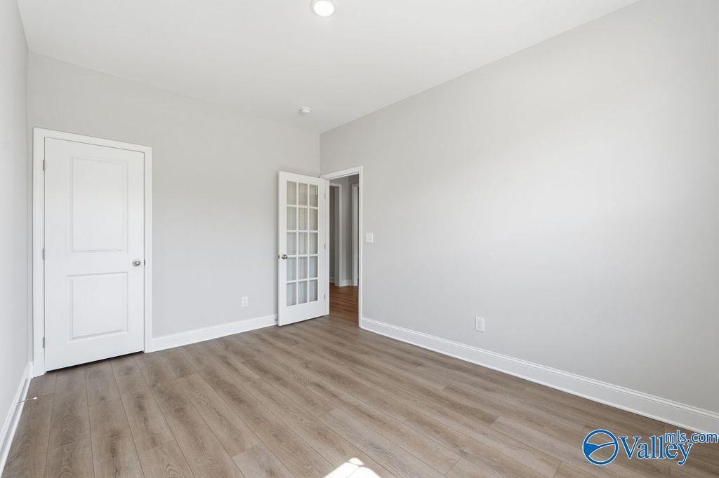 Spacious empty bedroom with light gray walls, white French doors, and oak LVP flooring in Davidson Homes The Harrison, Hartselle AL