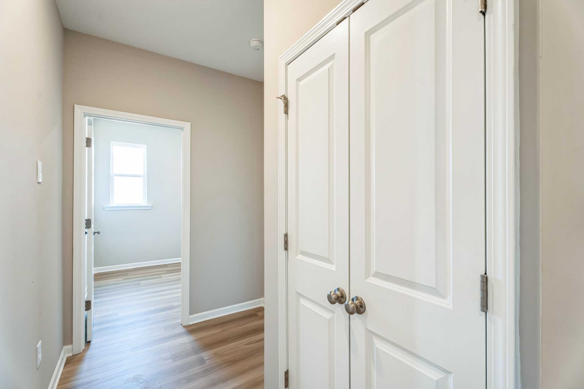 Spacious beige hallway with white double closet doors, open bedroom doorway, and hardwood floors at Anderson Lakes in Opelika Alabama