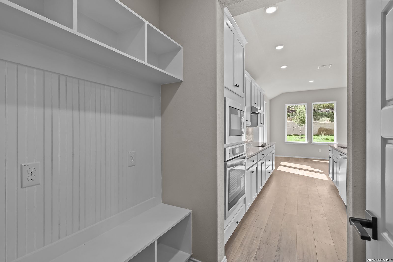 White mudroom bench with cubby storage beside kitchen with white cabinetry in Davidson Homes The Sequoia C, San Antonio
