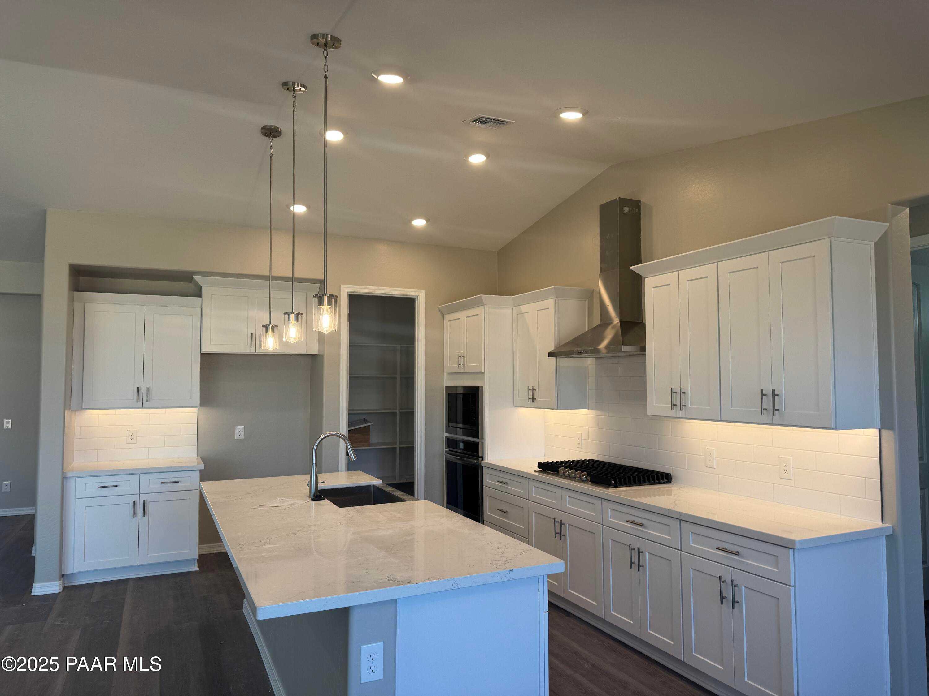 Modern white kitchen island with sink, stainless range hood, ovens, and pendant lights in Davidson Homes The Monarch E, Prescott AZ