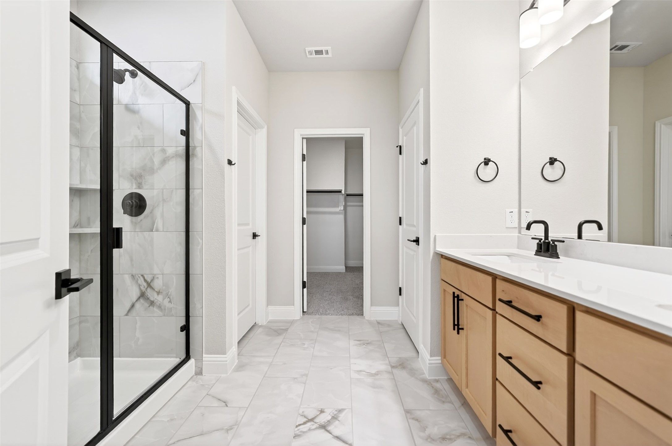 Modern primary bathroom with marble-style tile, glass shower, and walk-in closet in The Holly C plan, Anna, Texas.