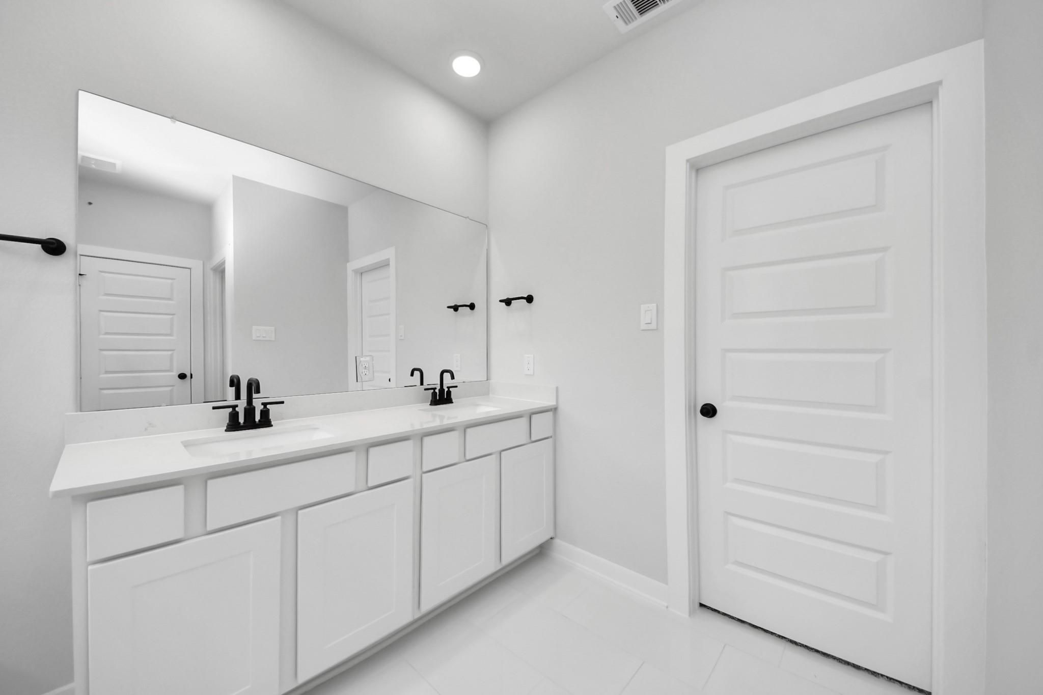 Modern double vanity with matte black fixtures in a Riviera C floor plan home at River Ranch Meadows in Dayton, Texas.