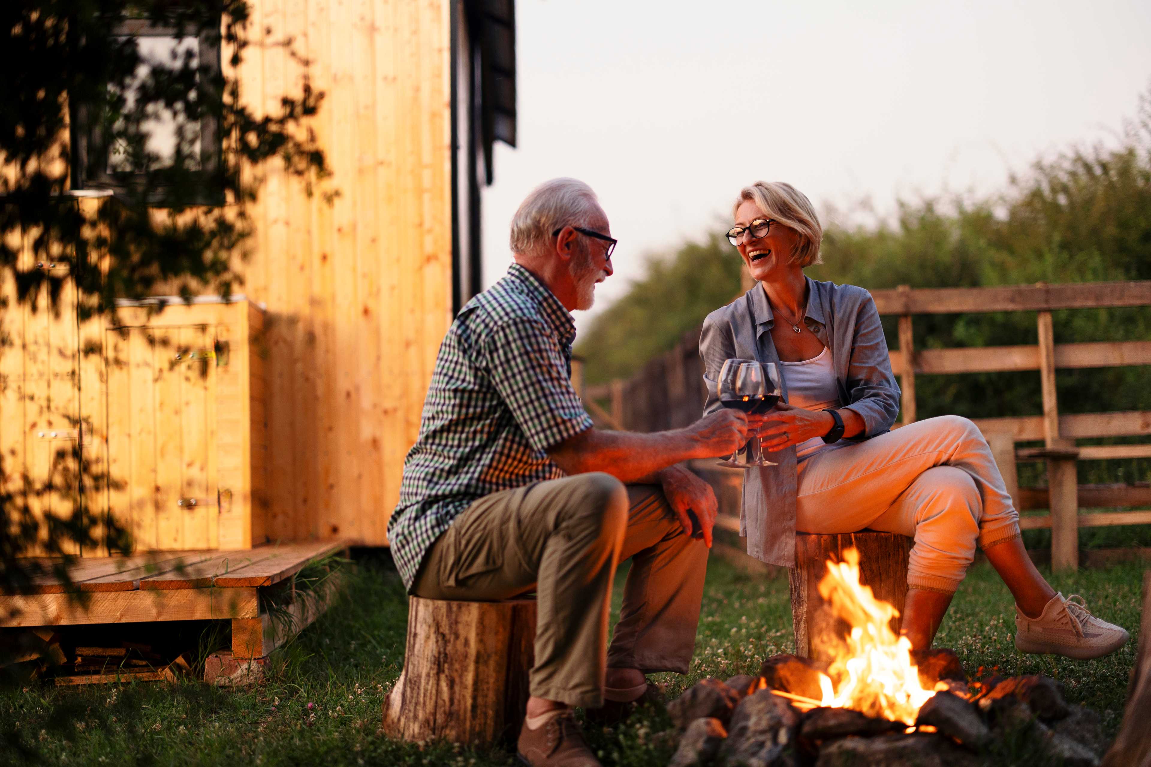 Senior couple toasting wine by campfire outside wooden cabin at Kelly Preserve in Loganville, Georgia