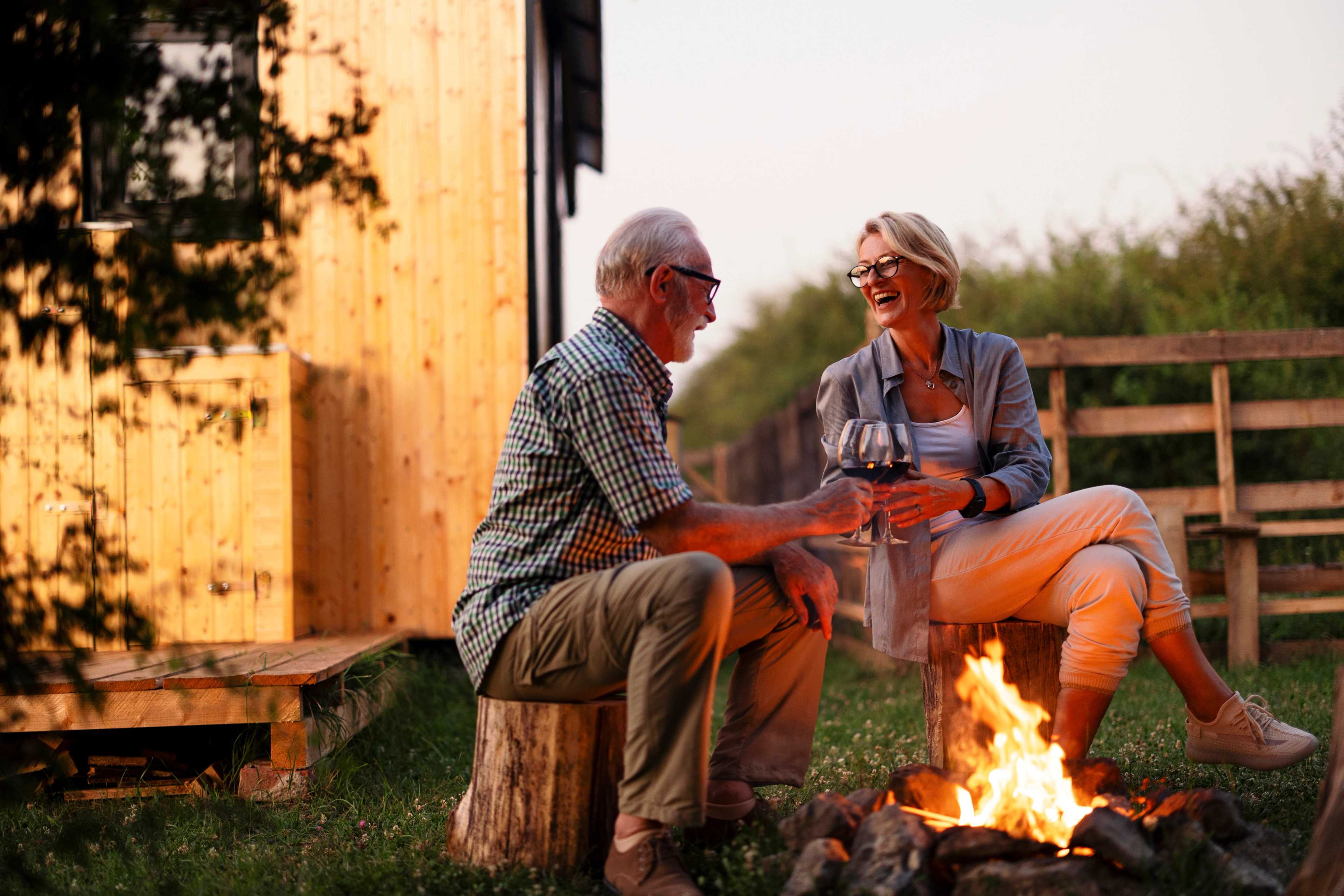 Senior couple toasting wine by campfire outside wooden cabin at Kelly Preserve in Loganville, Georgia