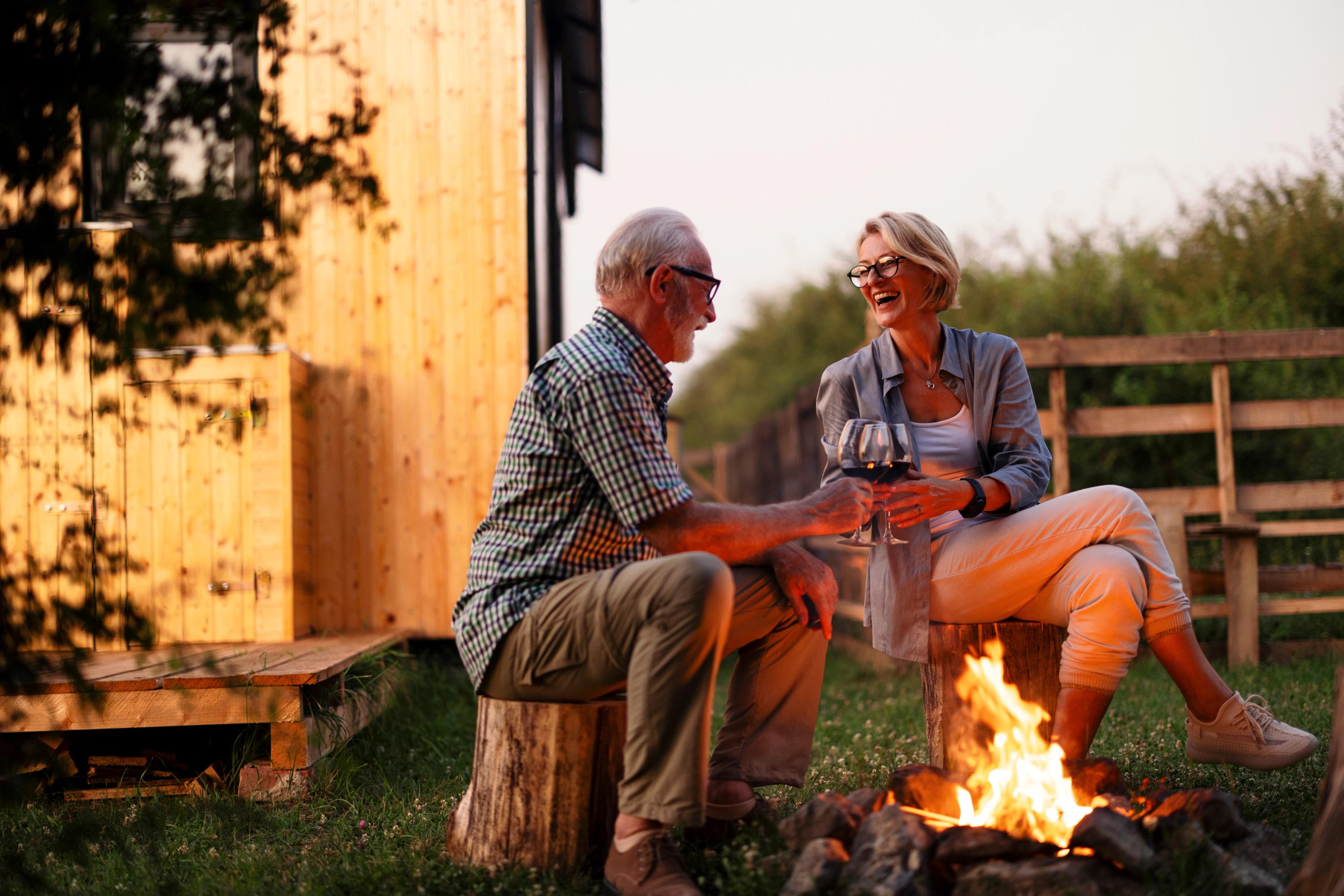 Senior couple toasting wine by campfire outside wooden cabin at Kelly Preserve in Loganville, Georgia