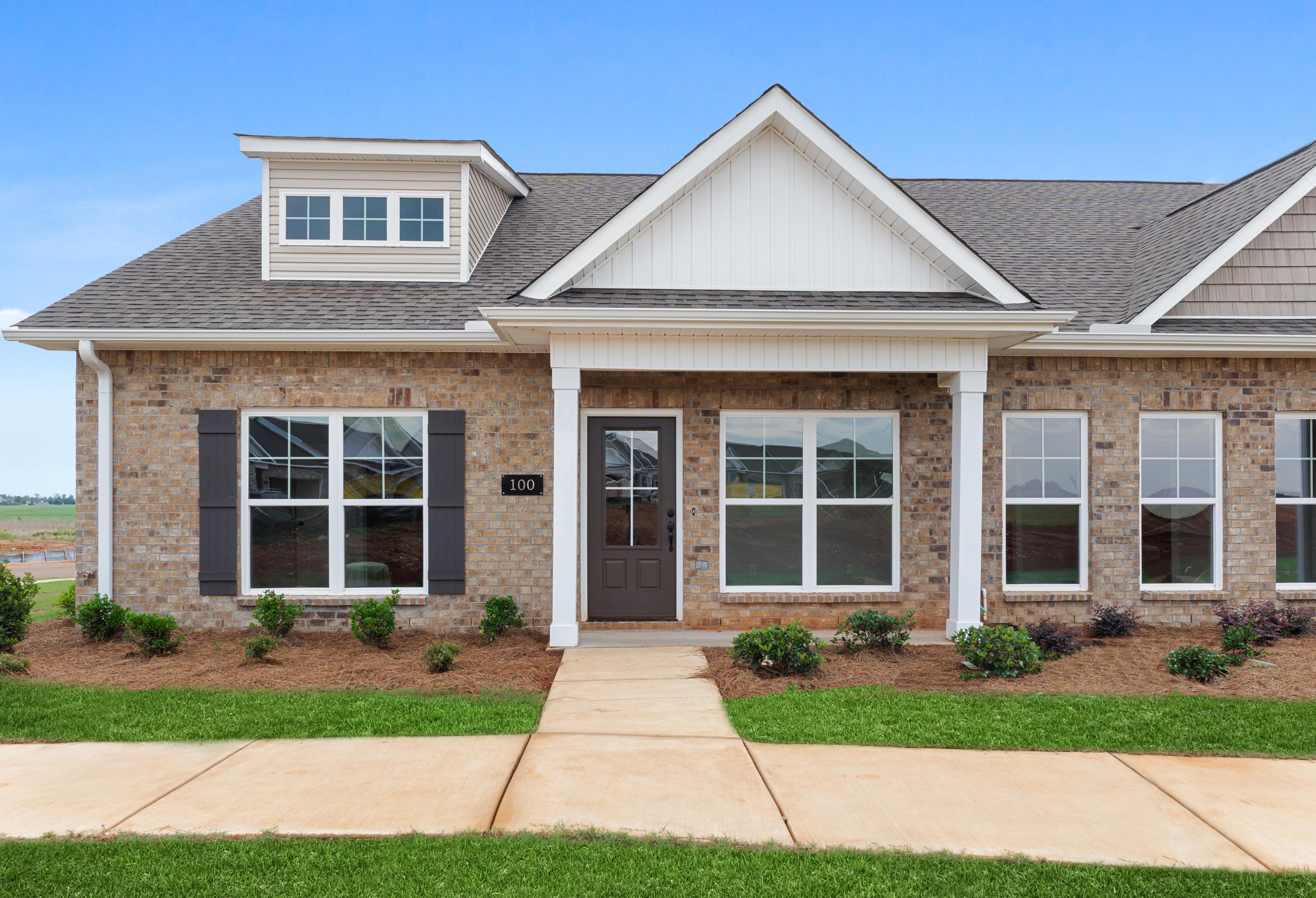 Two-story Copeland multi-family home elevation with brick facade, white gable roof, dormer window, covered porch, and landscaped entry