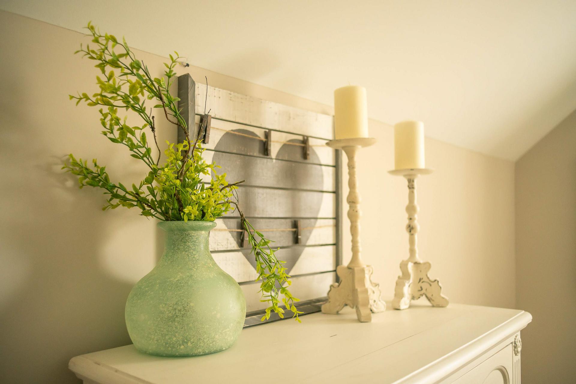 Rustic farmhouse decor with wooden heart frame, green vase of branches, white candlesticks on distressed dresser in Summer Pointe Madison AL home