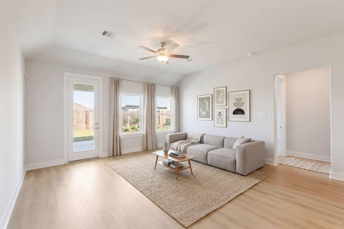 Bright family room with gray sofa, light wood floors, ceiling fan, and French doors to backyard in Davidson Homes The Luna J, Katy, Texas